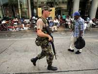 A soldier patrols a street in New Orleans, Saturday, Sept. 3, 2005, as people displaced by Hurricane Katrina wait for transportation out of the area