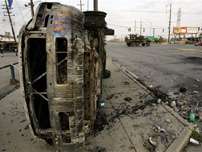 A military truck, right, drives past an overturned burned vehicle, in New Orleans, early Friday, Sept. 9, 2005.