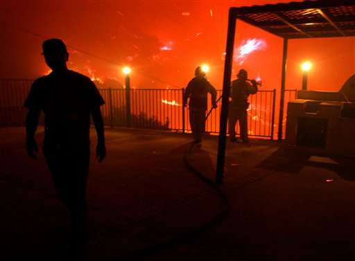 Los Angeles County firefighters protect a home from an approaching wildfire in the early morning hours of Thursday, Sept. 29, 2005, in the Chatsworth area of Los Angeles. Wind-driven brush fires are ringing huge areas of Southern California. Thousands of acres across four counties have been scorched. (AP Photo/Agustin Tabares)