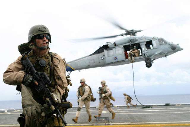 Sgt. Daniel Gurr is resolutely standing guard as fellow Marines move away from a helicopter that has just dropped them on the deck of a ship.