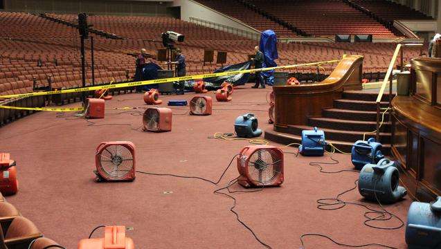 Fans dry carpet in the Conference Center after water from sprinkler heads overflowed to the auditorium floor. Flooding was limited to a 50-foot area in front of the podium but did not cause significant damage.
