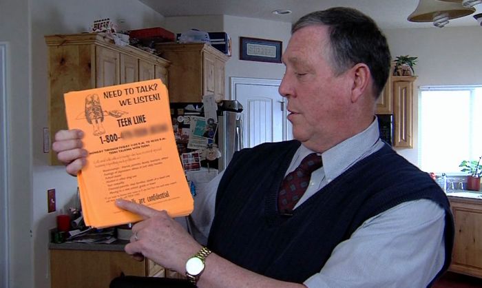 Dale Sheffer, a school counselor who played a role in promoting Teen Line, holds up a stack of fliers that explain the program and encourage teens to call the 1-800 number for help.