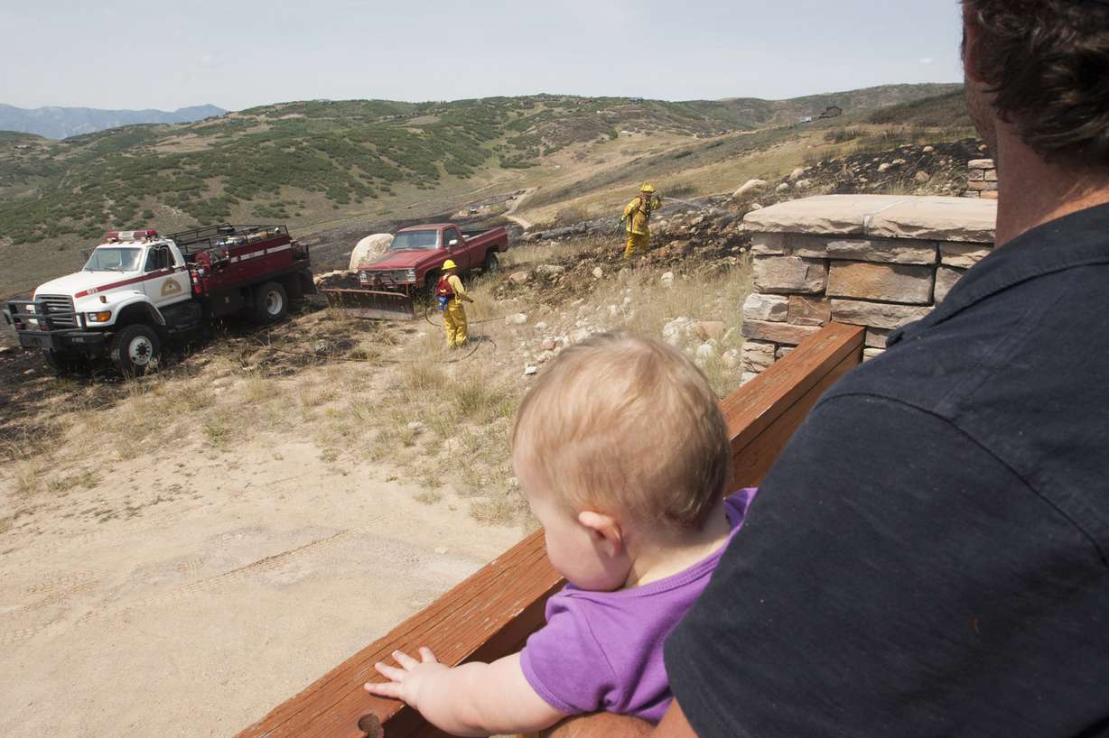 John Troilo watches as firefighters search for hot spots at 359 Park View Lane with Mena Troilo, 10 months, after a fire burned about 120 acres near the Rockport Estates community in Wanship, Saturday, July 26, 2014.