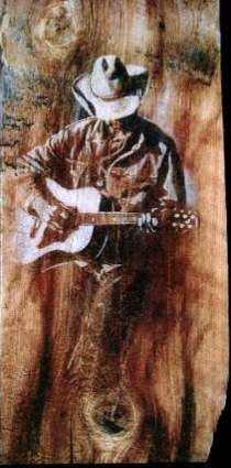 Painting, on old wathered barn wood with knots, of a cowboy playing his guitar, head down, face covered by his hat. Size approx 20" high x 10" wide. (Photo: Larry Nielson)