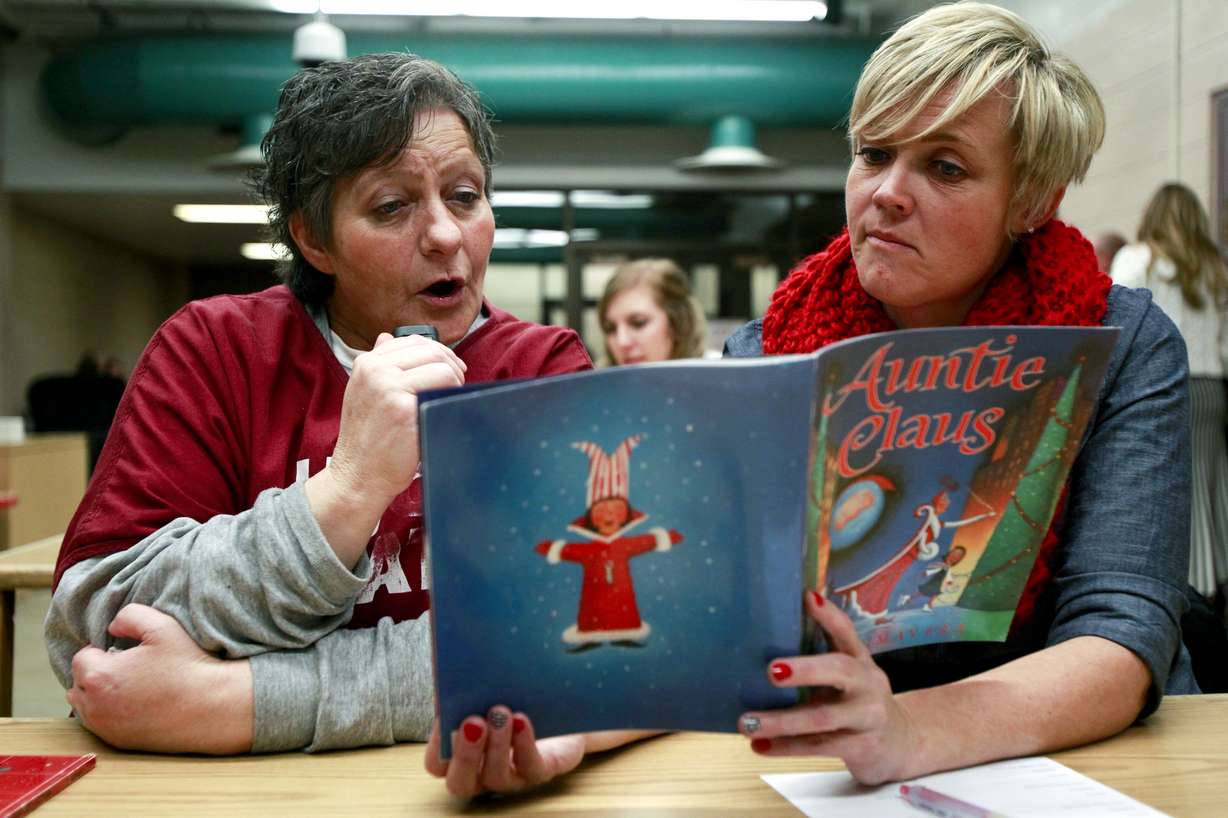 In this photo taken on Sunday, Dec. 14, 2014, Debbie Samples, left, records a children's story while Kristin Kmetzch holds up the book at the Timpanogos Women's Correctional Facility in Draper, Utah. Dressed in maroon jumpsuits, the women incarcerated at the facility take turns reading books about the adventures of a brown rabbit, a family of Berenstain Bears and a pig that eats a pancake. For 45 minutes, they read and giggle, feeding off each other's energy. Underneath their laughter, though, they each carry a weight. In addition to missing the big things, being in prison means they're missing out on the little things — like reading bedtime stories to the ones they love. (AP Photo/The Daily Herald, Ian Maule)