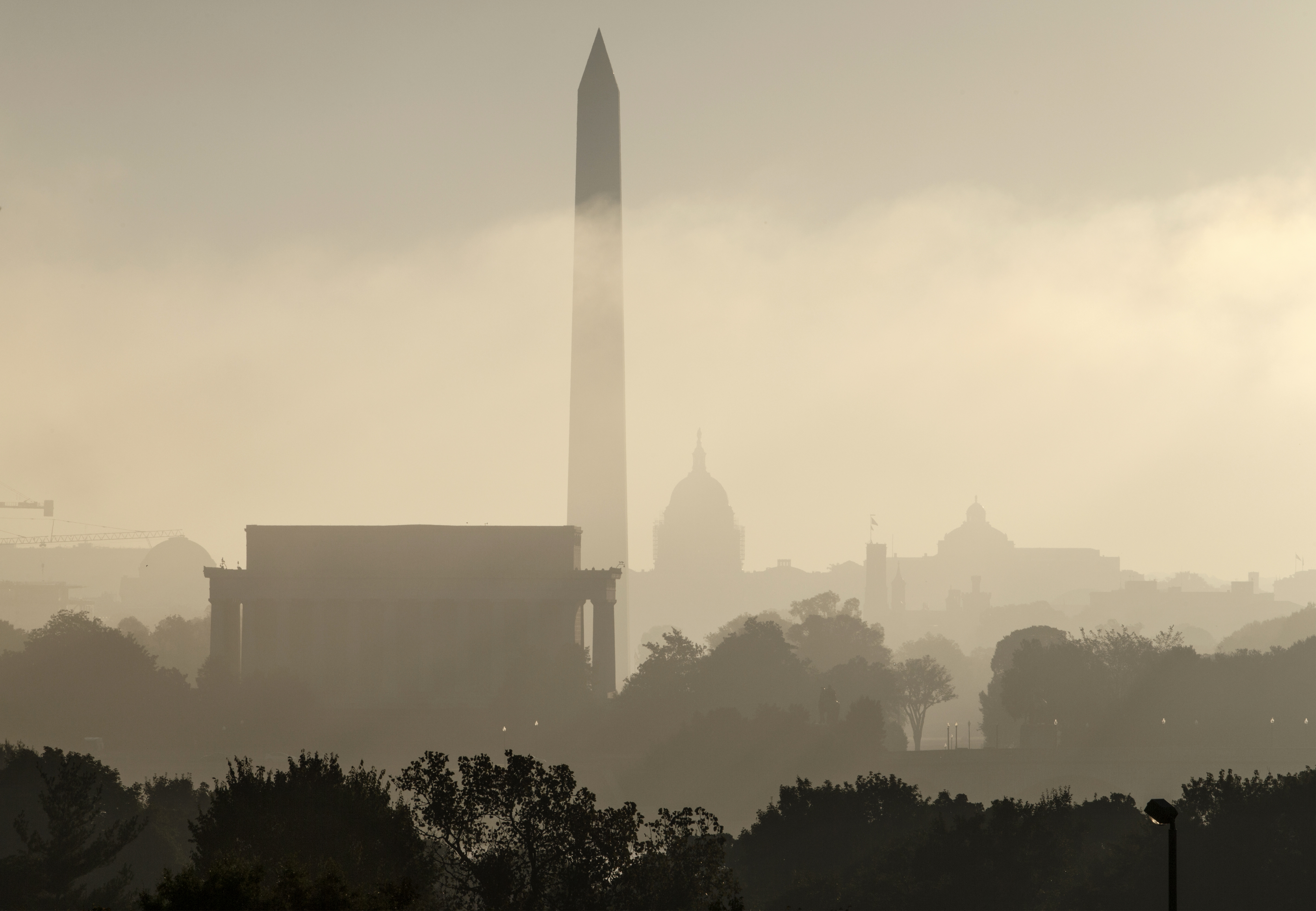 FILE- In this Sept. 26, 2014, photo, the monuments of Washington are silhouetted through the lifting fog over the nation's capitol as seen from an overlook in Arlington, Va. From left are, the Lincoln Memorial, Washington Monument, the Capitol, the Smithsonian Castle, and the Library of Congress. Government surveyors have determined a new height for the Washington Monument that's nearly 10 inches shorter than what has been thought for more than 130 years, officials will announce Monday, Feb. 16, 2015. (AP Photo/J. Scott Applewhite, File)