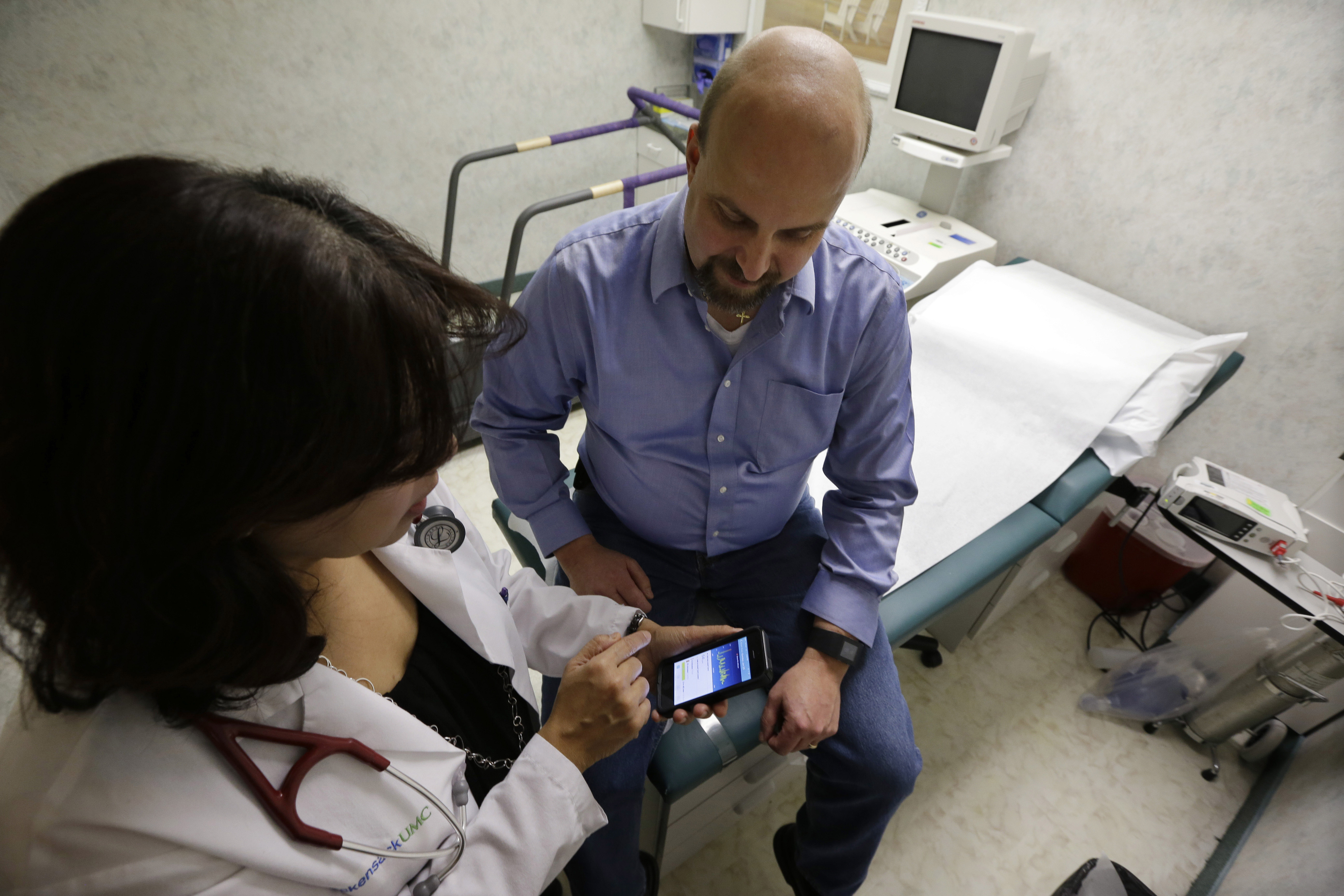 In this Thursday, Feb. 5, 2015 photograph, cardiologist Dr. Sarah Timmapuri, left, looks at data on a smart phone that is synchronized to a new Fitbit Surge on the wrist of patient Gary Wilhelm, 51, during an examination, in Hackensack, N.J. Wilhelm who works at Hackensack University Medical Center in New Jersey on payroll and finance technology, joined Hackensackâ€™s app test after he suffered a heart attack in October. (Mel Evans/Associated Press)