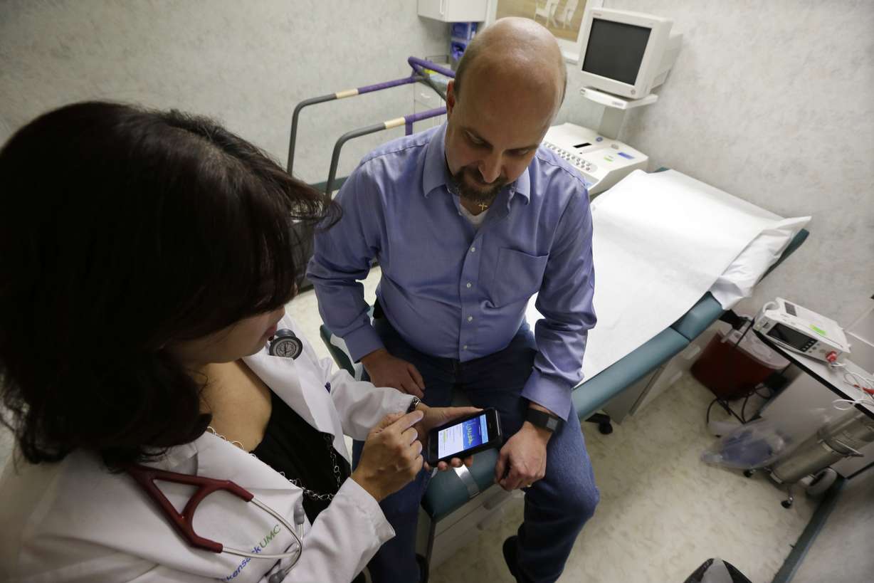 In this Thursday, Feb. 5, 2015 photograph, cardiologist Dr. Sarah Timmapuri, left, looks at data on a smart phone that is synchronized to a new Fitbit Surge on the wrist of patient Gary Wilhelm, 51, during an examination, in Hackensack, N.J. Wilhelm who works at Hackensack University Medical Center in New Jersey on payroll and finance technology, joined Hackensack’s app test after he suffered a heart attack in October. (Mel Evans/Associated Press)