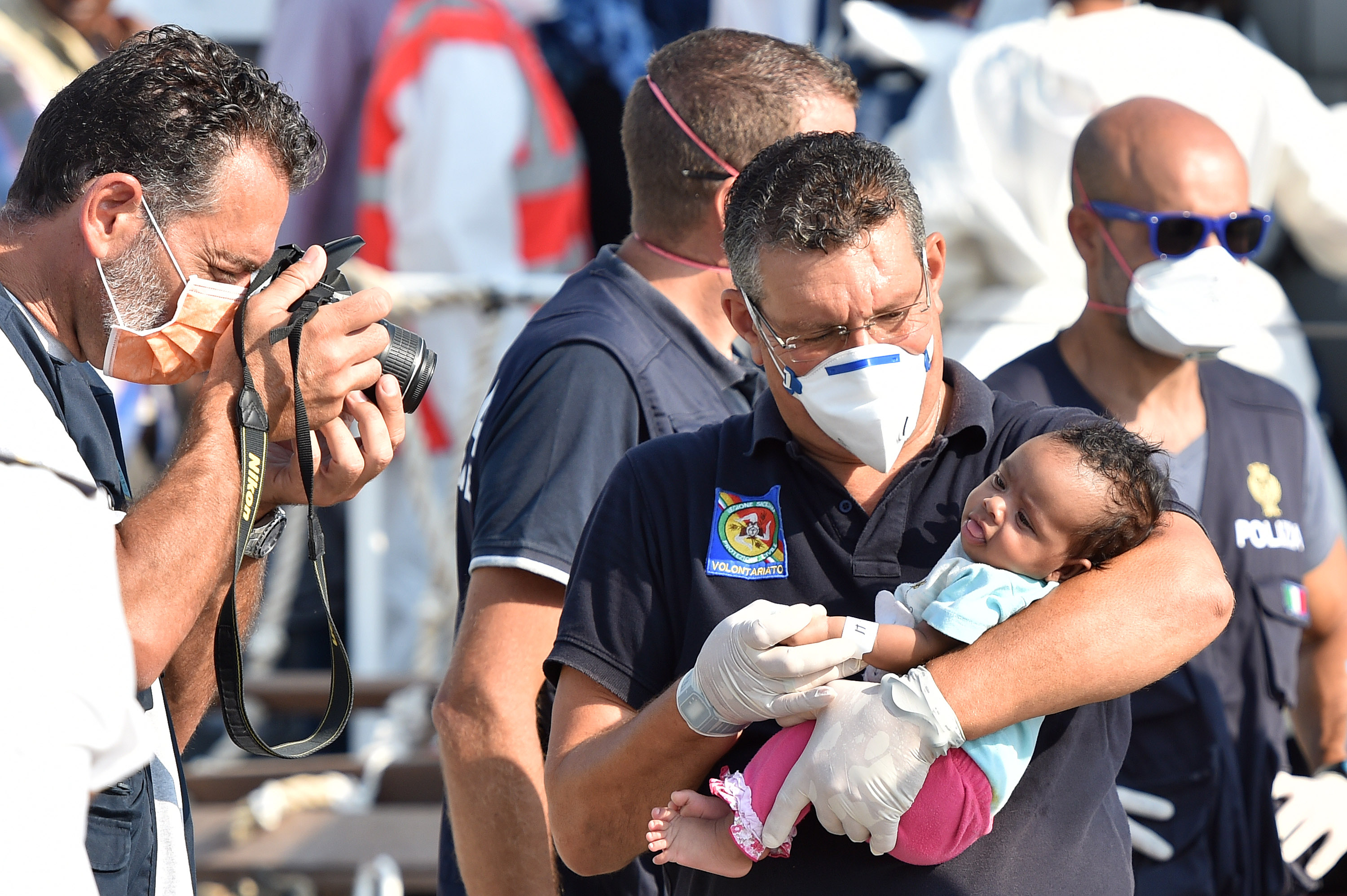 An Italian officer takes a photo of a baby as migrants disembark from the Italian Coast Guard ship Fiorillo in the harbor of Pozzallo, near Ragusa, Sicily, Italy, Friday, Aug. 7, 2015. On Thursday, 381 people were saved by the Italian coast guard before their boat sank off the Libyan coast. (AP Photo/Carmelo Imbesi)