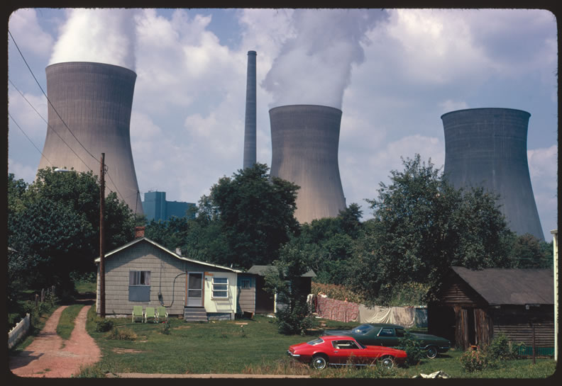 Water cooling towers of the John Amos Power Plant loom over a Poca, WV, home that is on the other side of the Kanawha River. Two of the towers emit great clouds of steam. Photo Credit: Harry Schaefer