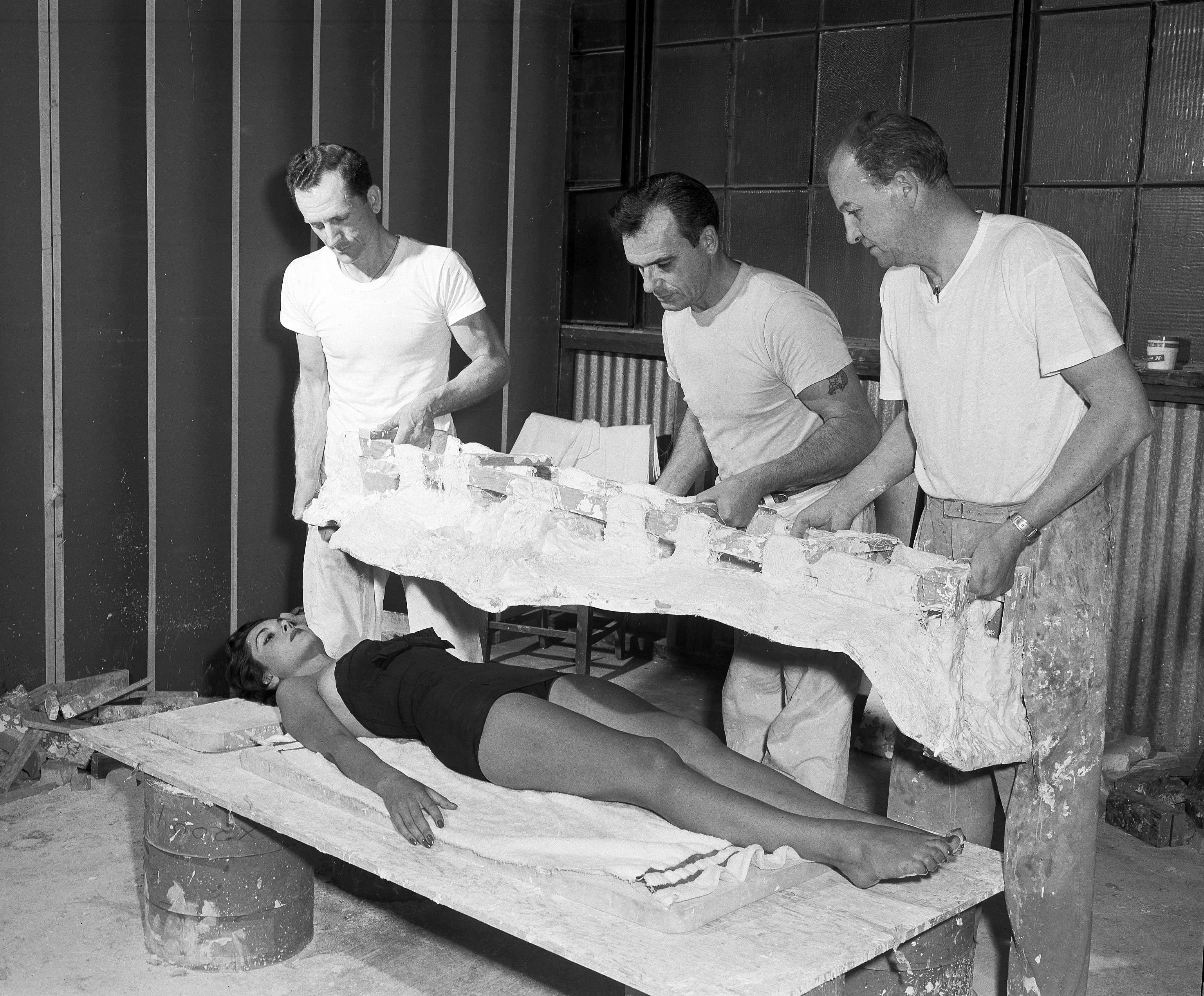 Actress Dana Wynter lies down on the job to serve as a mold for a plaster cast of her body in Hollywood, March 24, 1955. The cast was needed to make an image of her body for scenes in "The Body Snatchers." Miss Wynter, an English actress, will make her American movie debut in the film. Workers are, from left: John Podegracz, Lacey Cole and Don Post. (AP Photo)