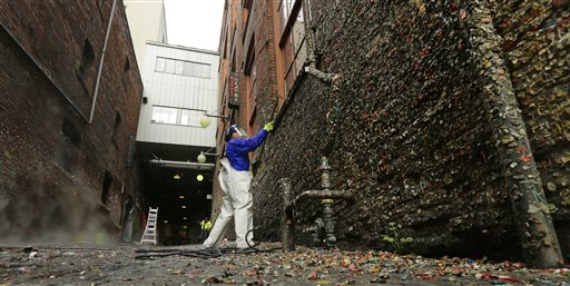 Fernando Soberania works to clean layers of gum from Seattle's famous "gum wall" at Pike Place Market, Tuesday, Nov. 10, 2015. Tourists and locals have been sticking their used chewing gum on the walls of a section of Post Alley for the past 20 years, and although the walls will be cleaned down to bare brick, officials expect the gum-sticking tradition will quickly return. (AP Photo/Ted S. Warren)