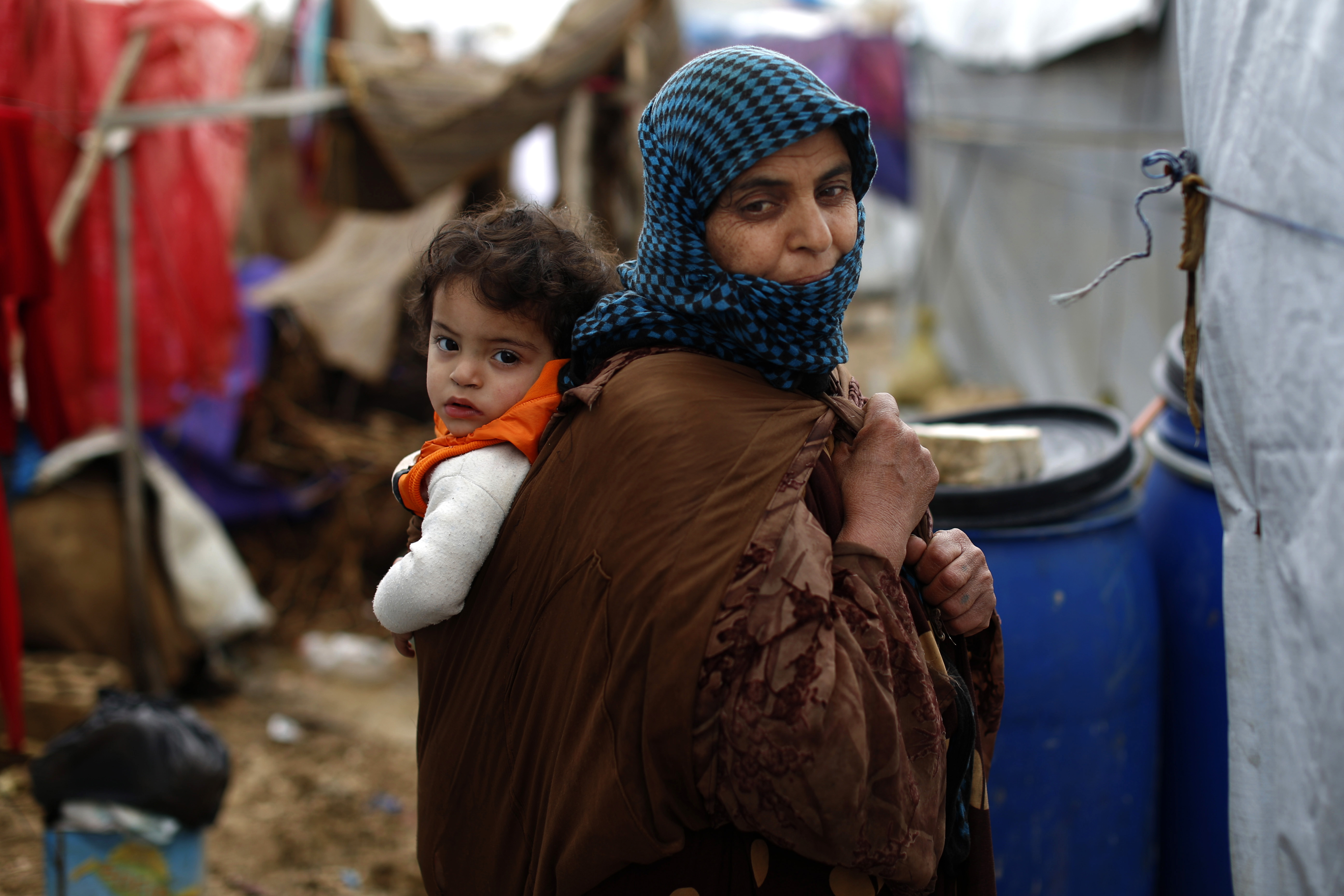 In this Monday, Jan. 4, 2016, file photo, a Syrian refugee carries a baby on her back at a refugee camp in the town of Hosh Hareem, in the Bekaa valley, east Lebanon. Photo: AP Photo
