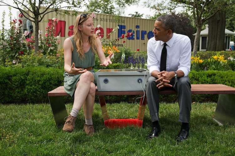President Obama chats with Sandra Richter, while sitting on the solar-powered bench she designed that charges mobile phones. (Official White House Photo by Pete Souza)