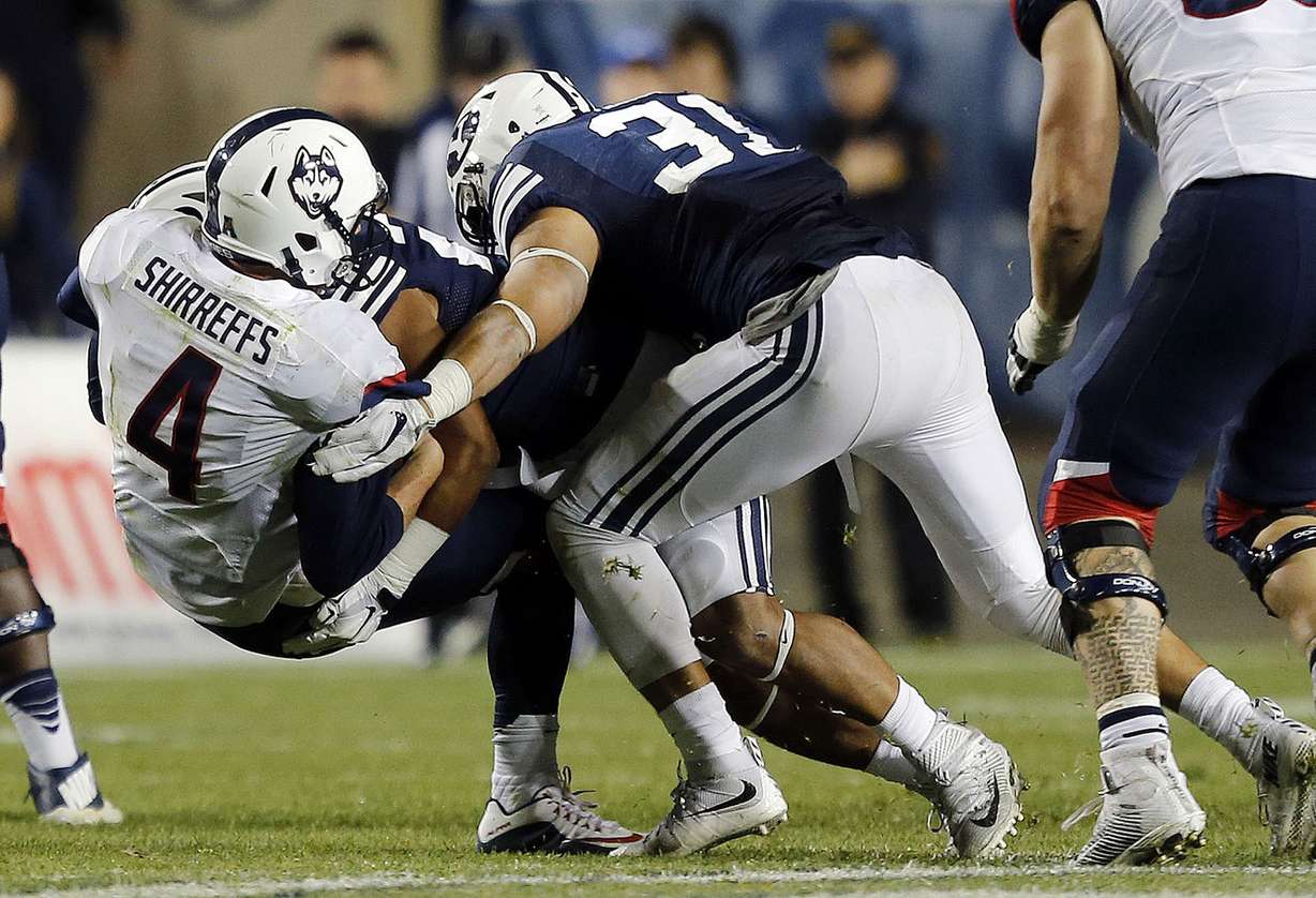 Quarterback Bryant Shirreffs (4) of the Connecticut Huskies is sacked by two BYU defenders during NCAA football in Provo, Friday, Oct. 2, 2015. At front right is Sae Tautu (31) of Brigham Young. (Photo: Ravell Call, Deseret News)