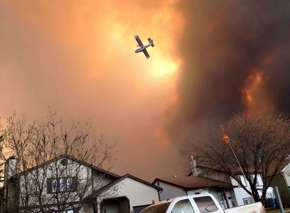 Smoke fills the air as a small plane flies overhead in Fort McMurray, Alberta, Tuesday, May 3, 2016. The entire population of the Canadian oil sands city of Fort McMurray, has been ordered to evacuate as a wildfire whipped by winds engulfed homes and sent ash raining down on residents. (Kitty Cochrane/The Canadian Press via AP)