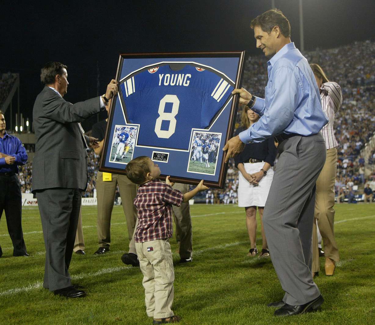 Braedon Young helps his dad Steve with a framed jersey BYU presented to Young at Halftime of the BYU-Georgia Tech football game where they retired his jersey. BYU President Cecil O. Samuelson at left. Aug. 28, 2003. (Photo: Stuart Johnson, Deseret News)