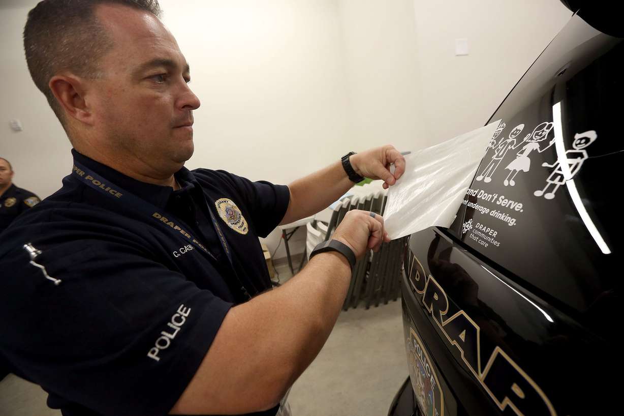 Draper Police Sgt. Chad Carpenter adheres a new underage alcohol prevention sticker to a patrol car after attending the Pledge to Prevent Underage Drinking forum in Draper on Wednesday, July 27, 2016. (Photo: Kristin Murphy, Deseret News)