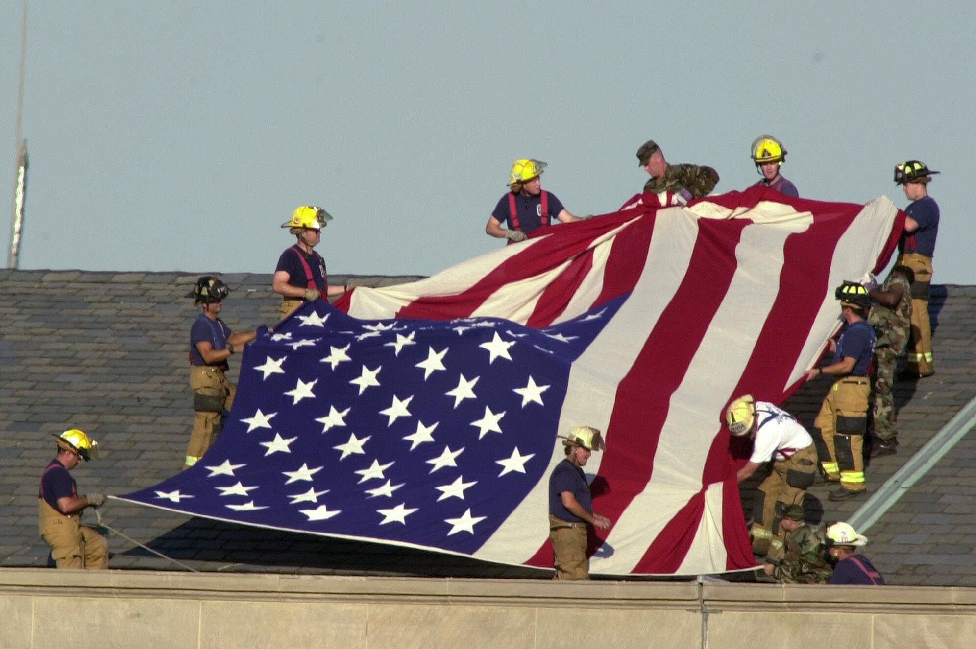 Firefighters on the roof of the Pentagon, Wednesday, Sept. 12, 2001, get ready to unfurl an American flag as President Bush visits the area of the Pentagon damaged by a terrorist, who crashed a hijacked airliner into the building on Sept. 11. (Ron Edmonds, AP Photo)