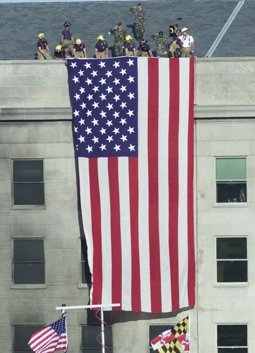 Firefighters unfurl an American flag from the roof of the Pentagon Wednesday, Sept. 12, 2001, as President Bush visits the area of the Pentagon where an airliner, hijacked by terrorists, crashed into the building on Sept. 11. (Ron Edmonds, AP Photo)