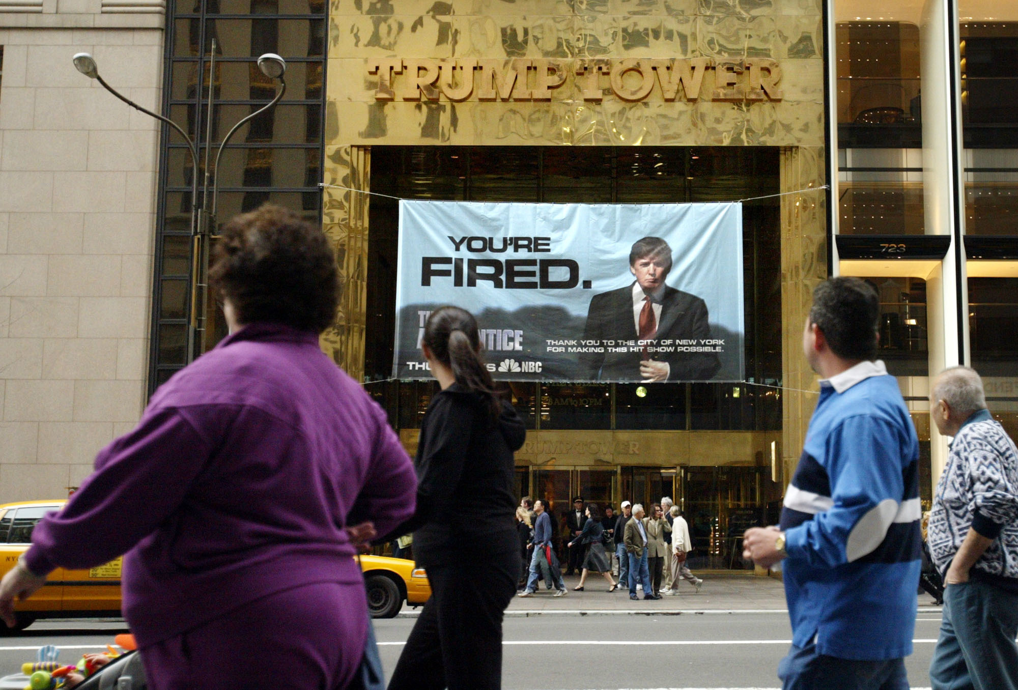 FILE - In this March 27, 2004 file photo, passersby look at a sign from Donald Trump's television show, "The Apprentice," hung on the Trump Tower in New York. (Bebeto Matthews, AP Photo, File)