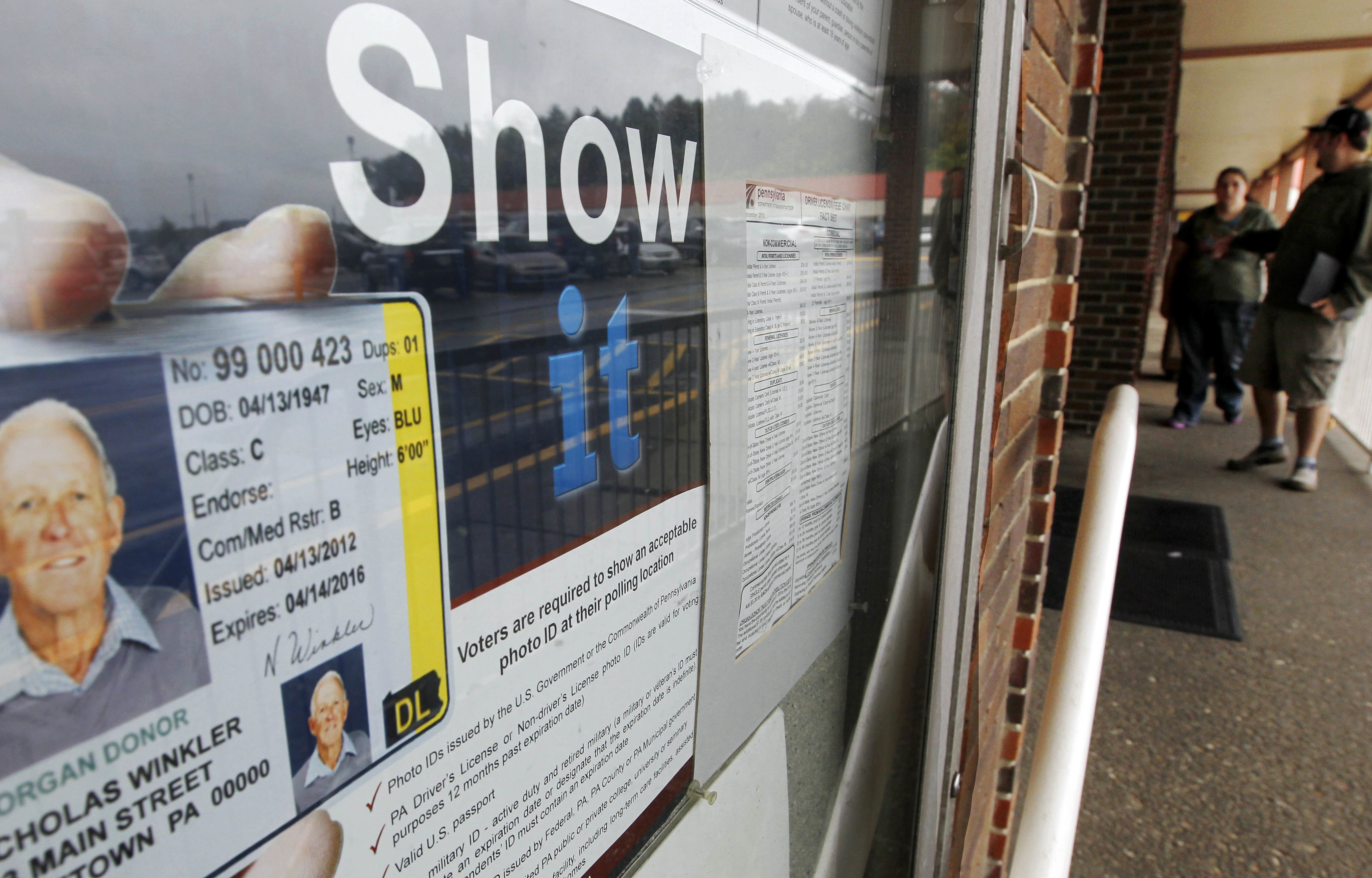 People pass the signs telling of the requirement for voters to show an acceptable photo ID to vote as they head into the the Penndot Drivers License Center in Butler, Pa. The U.S. Homeland Security Department said Monday it will delay enforcement of rules requiring Americans to get new identification cards in order to board airplanes or enter a federal building.