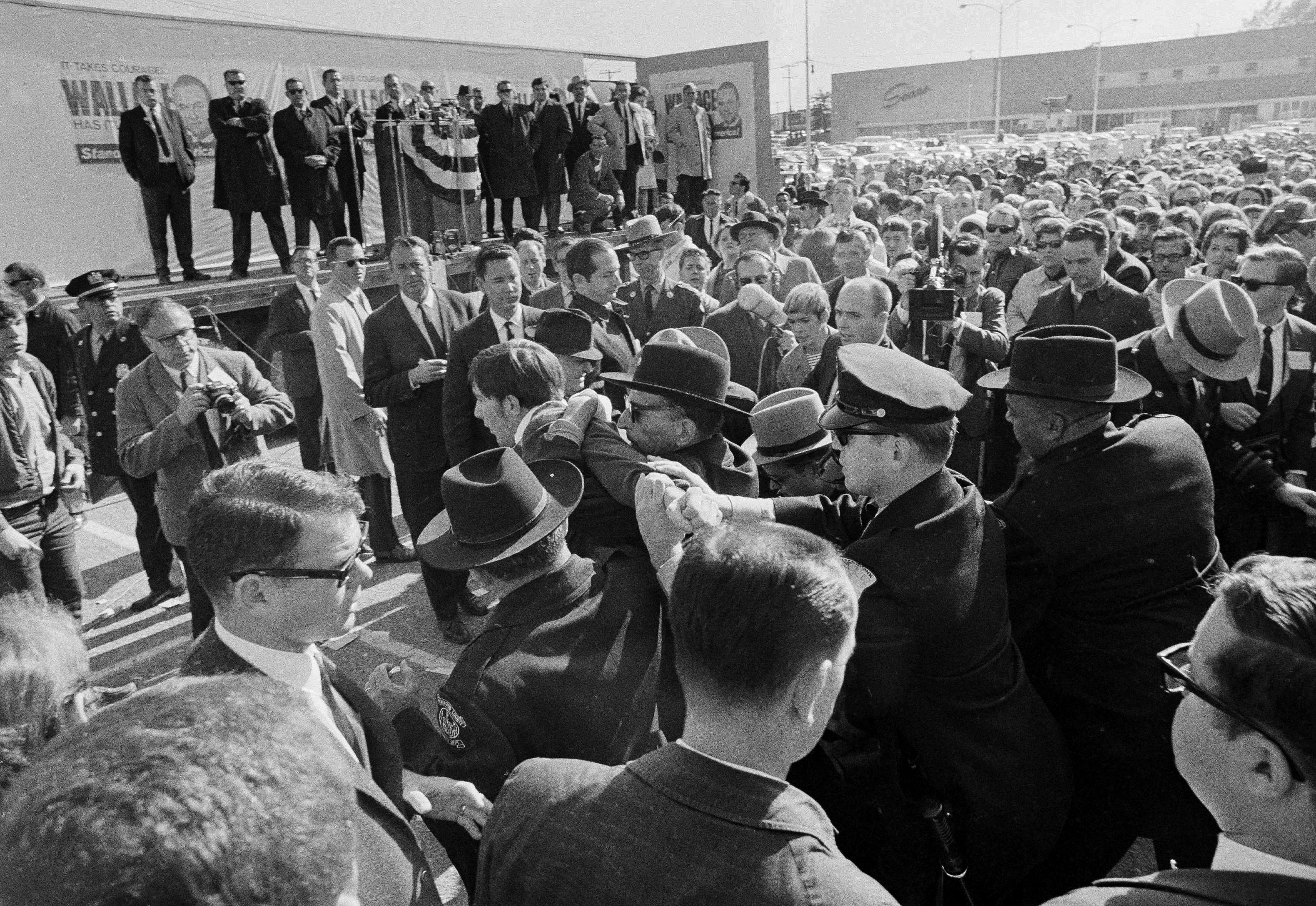 An ant-Wallace demonstrator is taken away by police as Third Party presidential candidate George Wallace leans behind the rostrum on the stage while addressing a crowd at a shopping center in Hagerstown, Md., Oct. 31, 1968. (Paul Vathis, AP Photo)