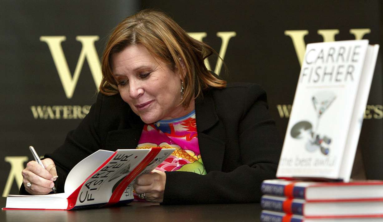 In this Friday, Feb. 20, 2004 file photo, author Carrie Fisher autographs her new book "The Best Awful" at a promotional event in London. On Tuesday, Dec. 27, 2016, a publicist said Fisher has died at the age of 60. (AP Photo/John D. McHugh, File)