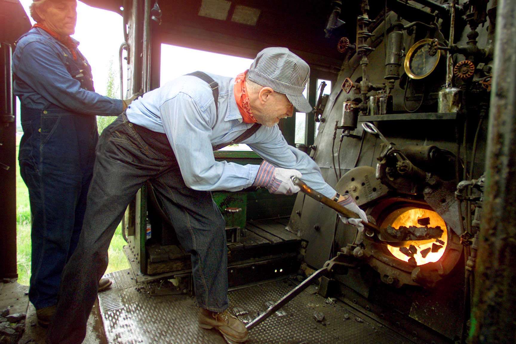 Ken Mcconnell (Conductor) watches over Gib Twyman as he shovels coal in the steam engine of the on the Heber Creeper in 2001. (Photo: Deseret News Archives)