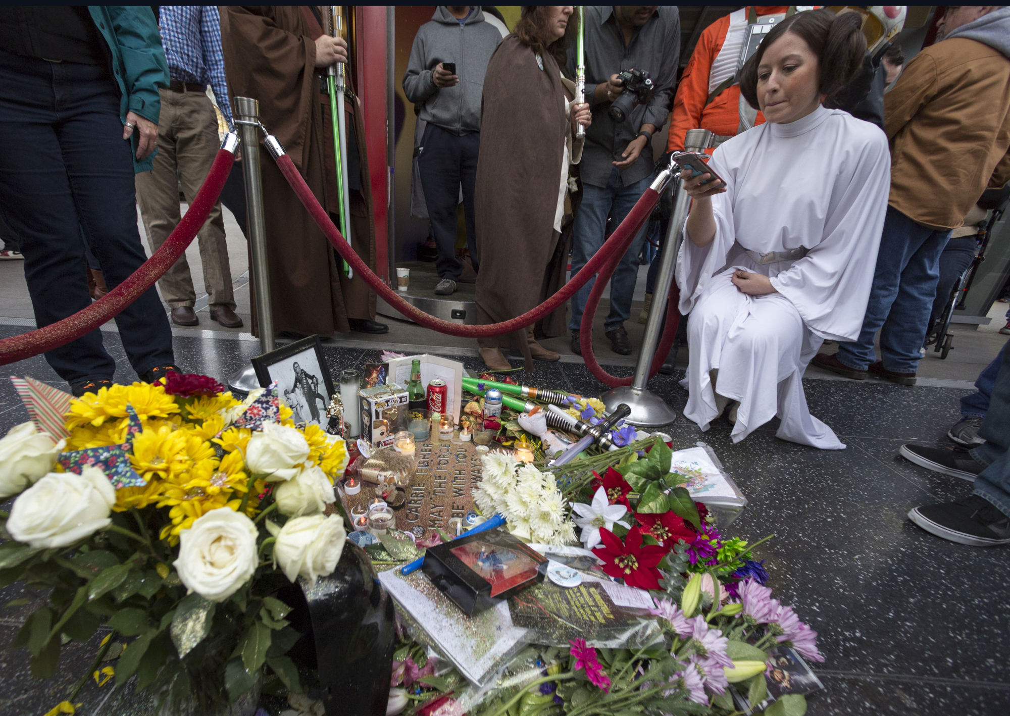 Victoria Schmidt, right, dressed as Princess Leia, in honor of actress Carrie Fisher, takes photos of an impromptu memorial created on a blank Hollywood Walk of Fame star in the Hollywood section of Los Angeles, Saturday, Dec. 31, 2016. (Damian Dovarganes, AP Photo, File)