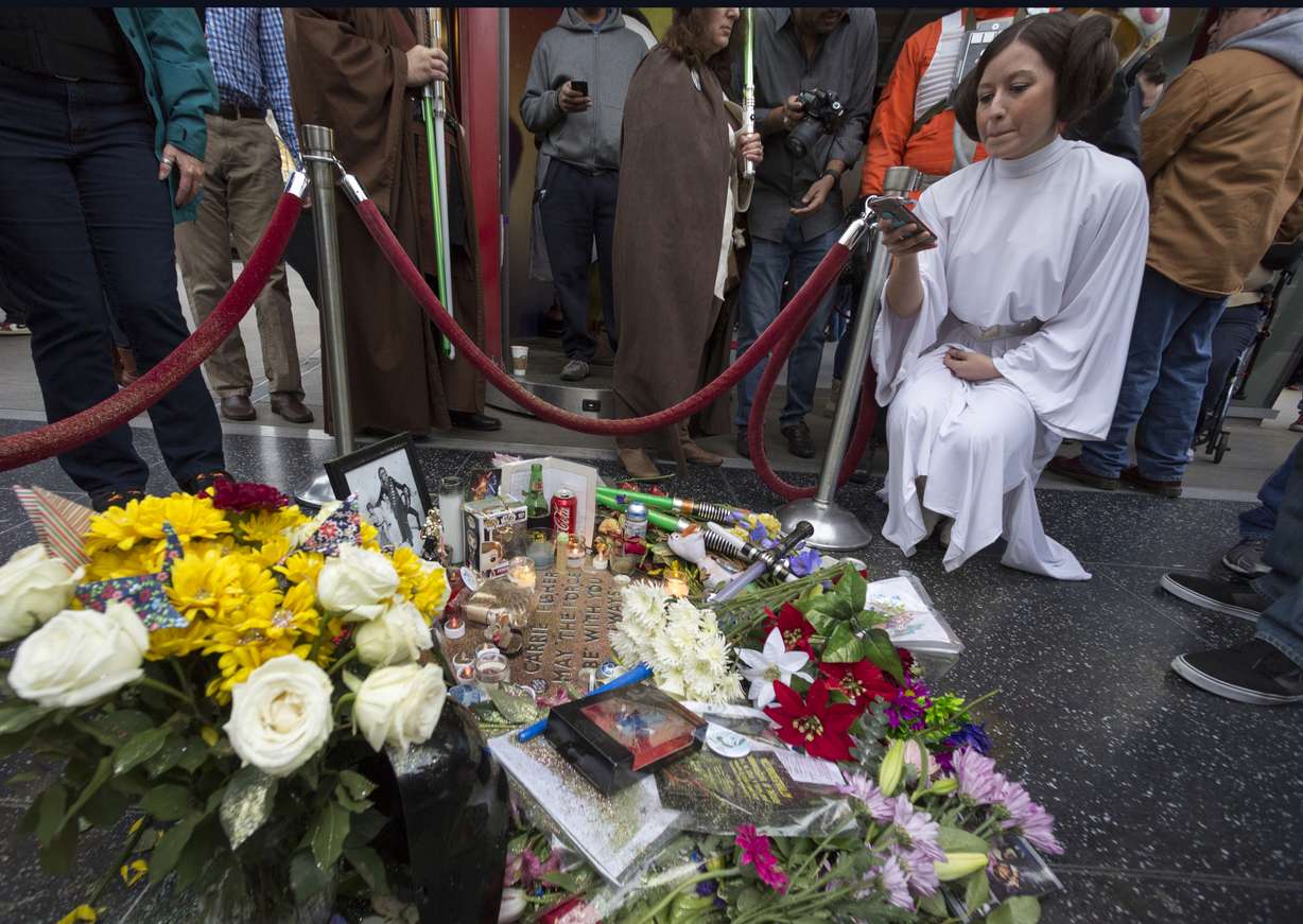 Victoria Schmidt, right, dressed as Princess Leia, in honor of actress Carrie Fisher, takes photos of an impromptu memorial created on a blank Hollywood Walk of Fame star in the Hollywood section of Los Angeles, Saturday, Dec. 31, 2016. (Damian Dovarganes, AP Photo, File)