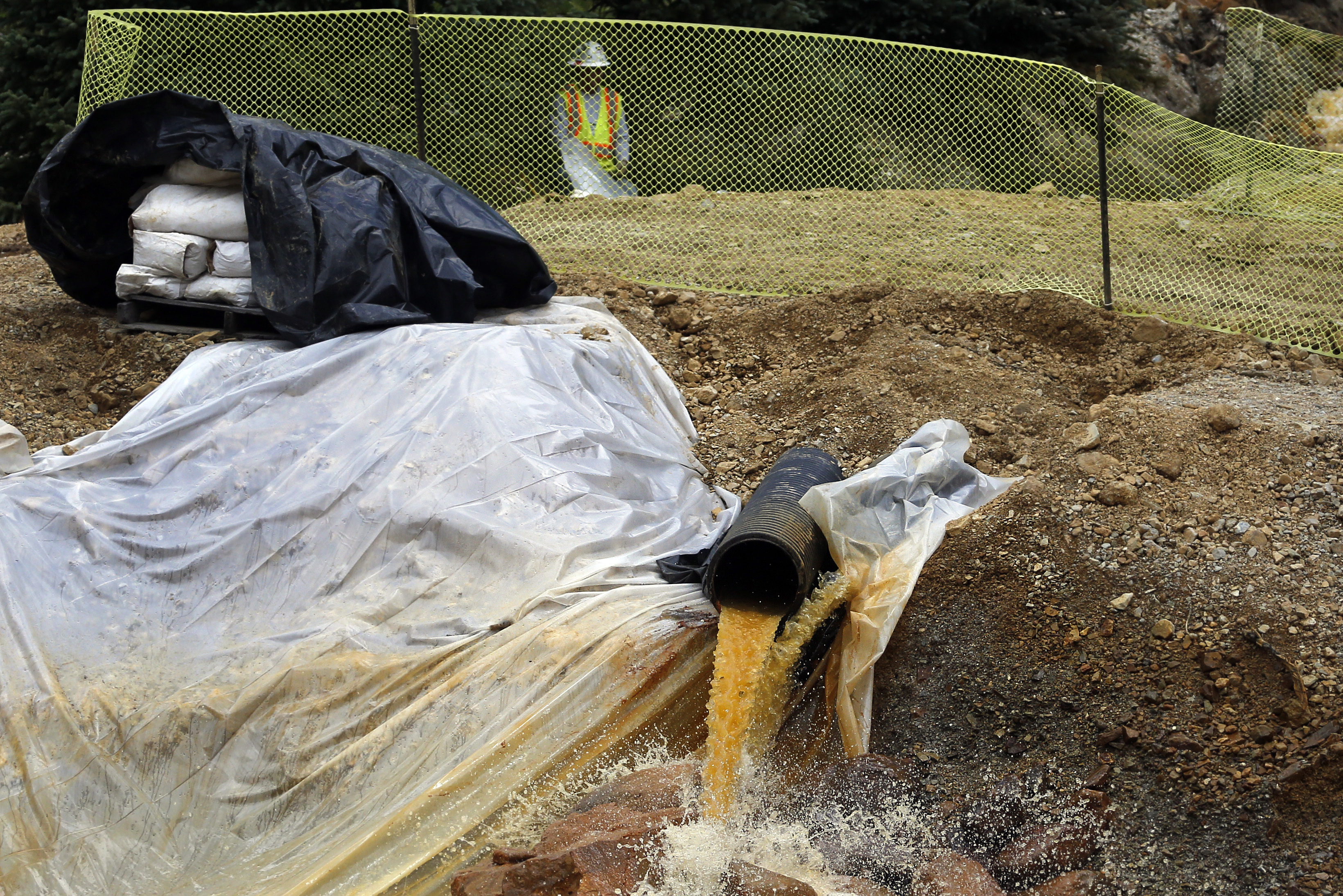 In this Aug. 12, 2015 photo, an Environmental Protection Agency contractor works on the cleanup in the aftermath of the blowout at the Gold King Mine, overseeing water flowing from the mine into a series of sediment retention ponds, mitigating damage from the spill of toxic wastewater, outside Silverton, Colo. Farmers, business owners and residents initially said they suffered $1.2 billion in lost income, property damage and personal injuries from the 2015 spill at the Gold King Mine. The total now appears to be about $420 million after attorneys for a handful of New Mexico property owners slashed their claims by $780 million. (AP Photo/Brennan Linsley)