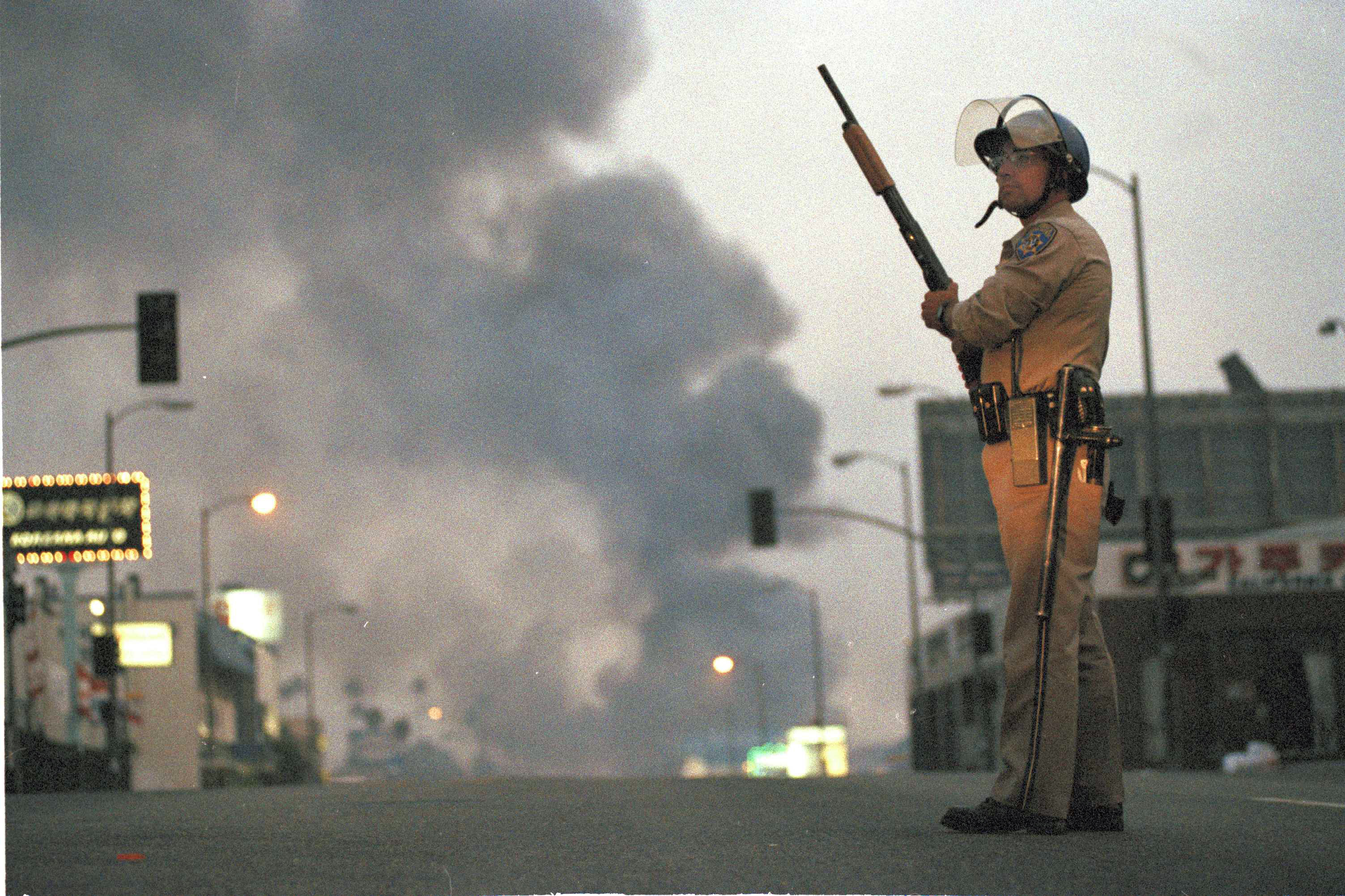 A California Highway Patrol officer stands guard at Ninth Street and Vermont Avenue in Los Angeles as smoke rises from a fire further down the street, April 30, 1992. (David Longstreath, AP Photo)