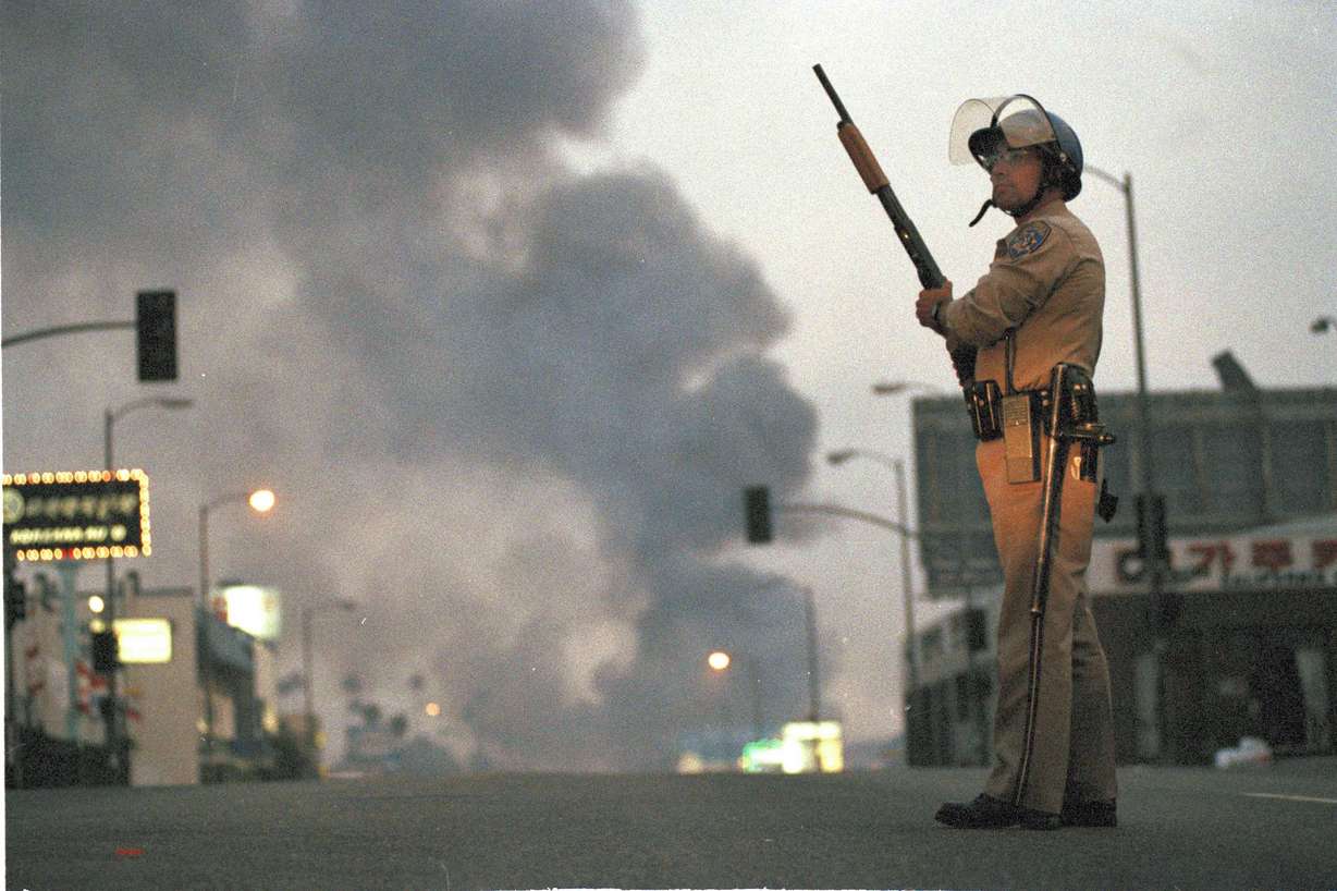 A California Highway Patrol officer stands guard at Ninth Street and Vermont Avenue in Los Angeles as smoke rises from a fire further down the street, April 30, 1992. (David Longstreath, AP Photo)