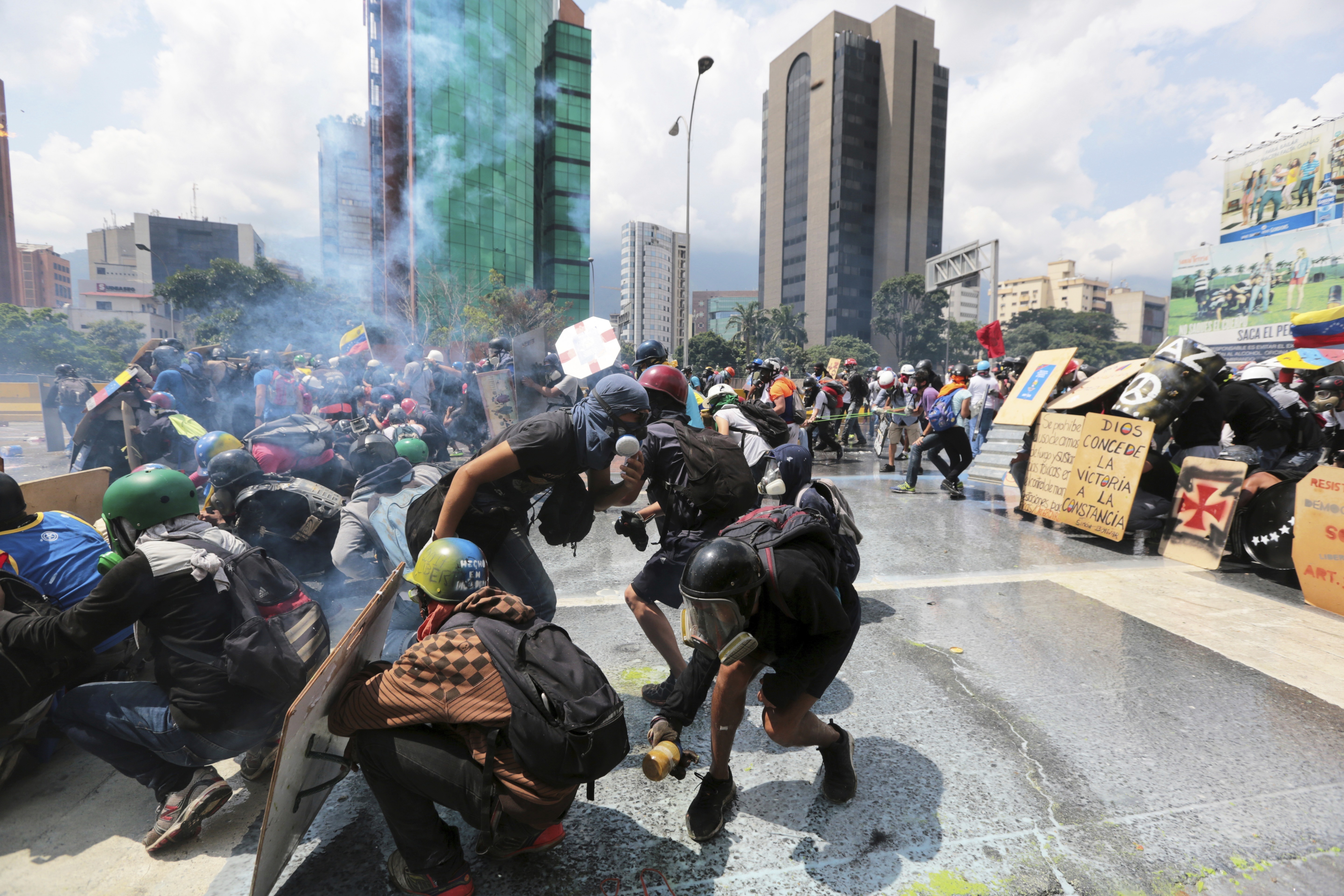 In this May 10, 2017 photo, a demonstrator, right center, holds a glass bottle filled with feces, known as a "puputov," to throw at Bolivarian National Guards during clashes with security forces at an anti-government protest in Caracas, Venezuela. In front of the protesters stands a line of officers equipped with bulletproof vests, visored helmets and plastic shields to protect themselves from the rocks and "puputovs" that some demonstrators throw their way. (AP Photo/Fernando Llano)