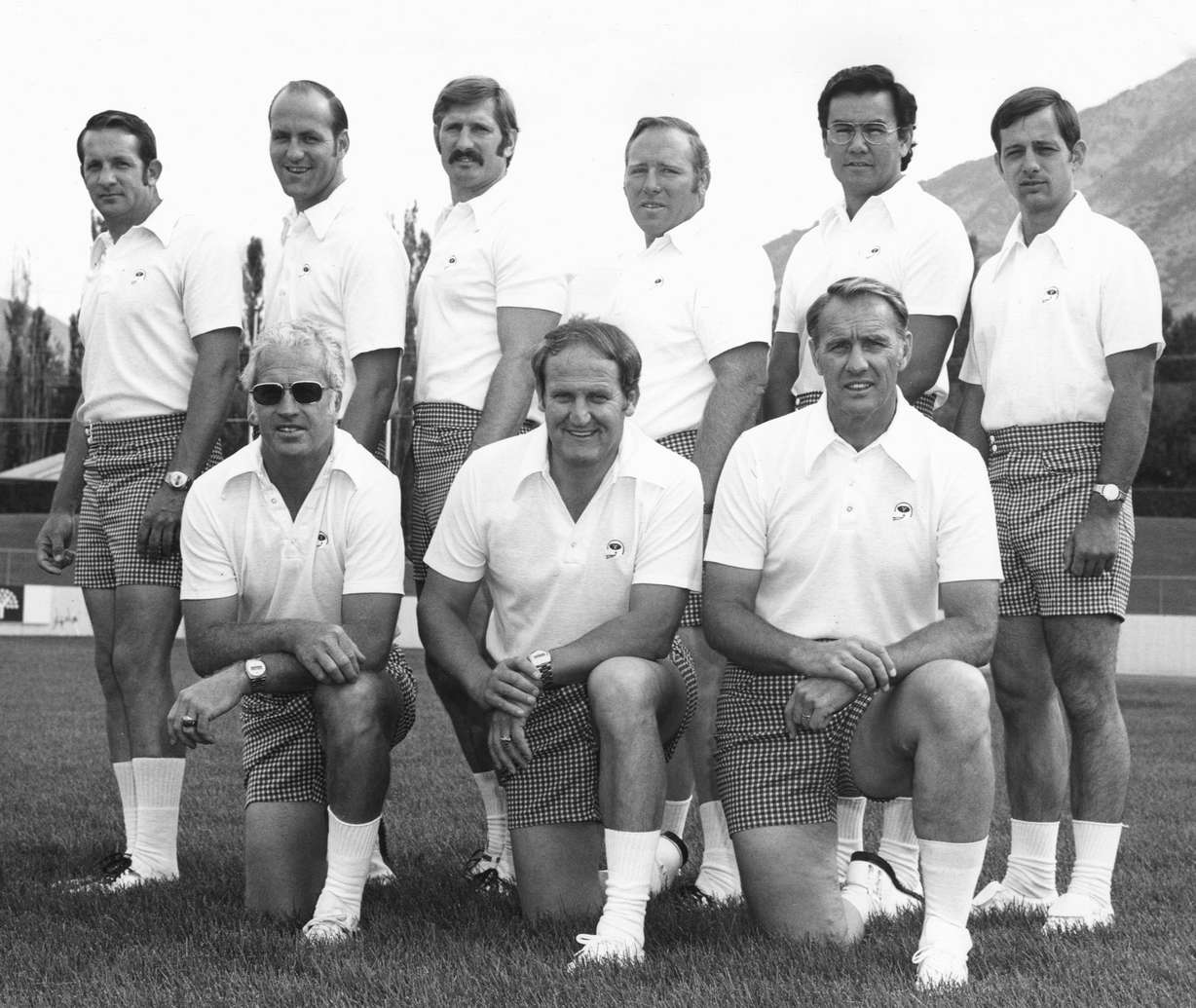 BYU's 1975 football coach staff poses for a photo. Standing row: Dwain Painter, Mel Olson, Fred Whittingham, Sr., Tom Ramage, Norm Chow, Garth Hall. Kneeling row: Dick Felt, LaVell Edwards, Dave Kragthorpe. (Photo: Mark Philbrick, BYU)