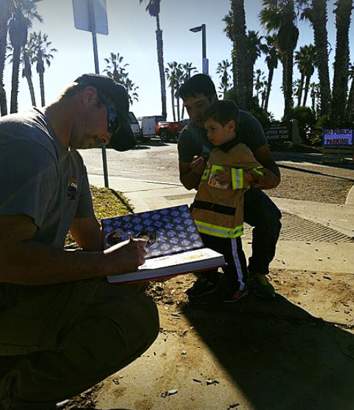 A boy in a firefighter's jacket asks members of the Weber Fire District to sign a book in Santa Barbara, California. (Photo: Weber Fire District)