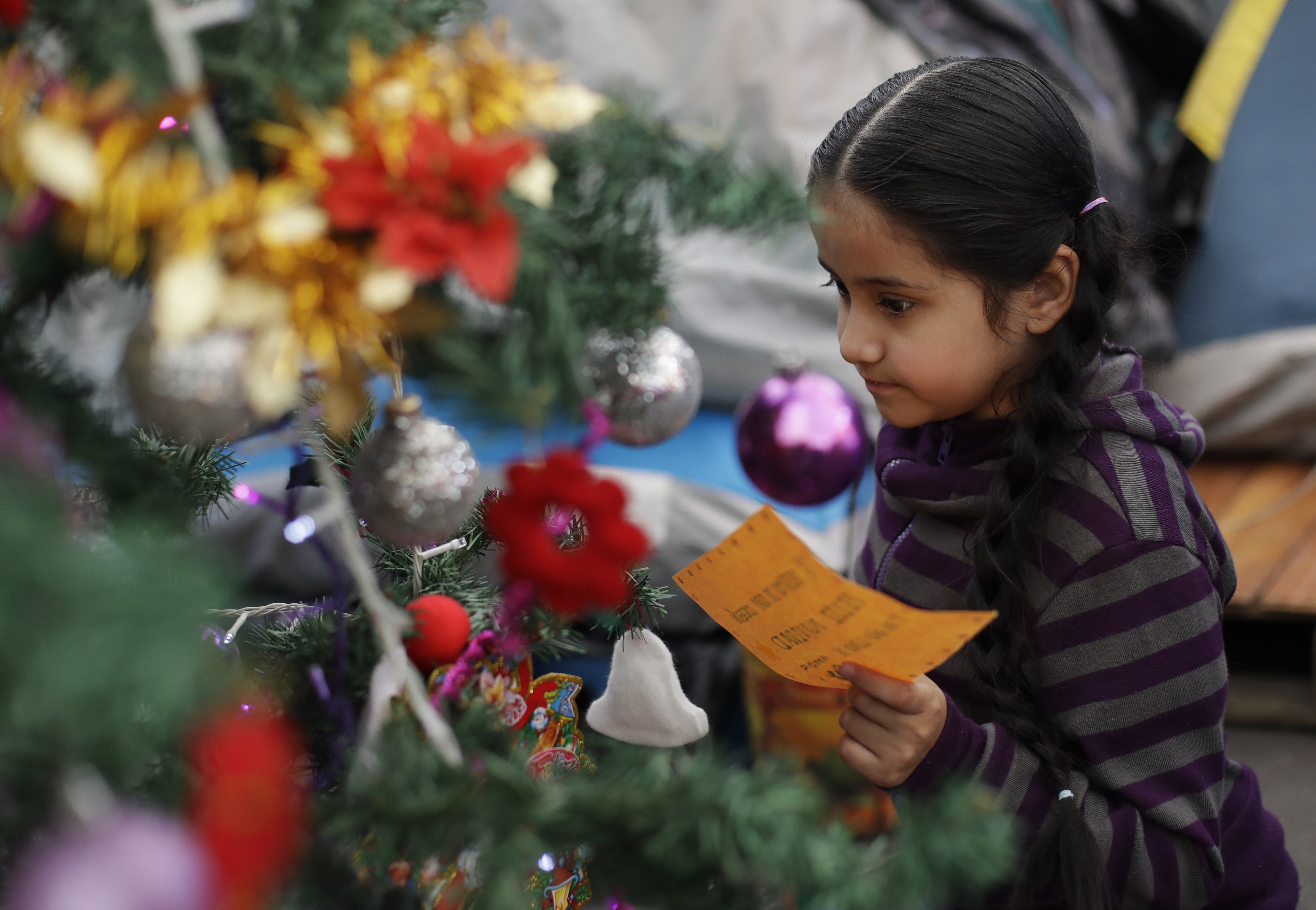 A girl reads a note placed on a Christmas tree inside a tent camp where residents of Calle Independencia 18 have been living since their apartment building was heavily damaged in the Sept. earthquake, in Mexico City, Friday, Jan. 5, 2018. In Mexico, it is customary for gifts to be given on Three Kings Day, Jan. 6, rather than Christmas Day. Children leave notes on the tree to request a present. (AP Photo/Rebecca Blackwell)