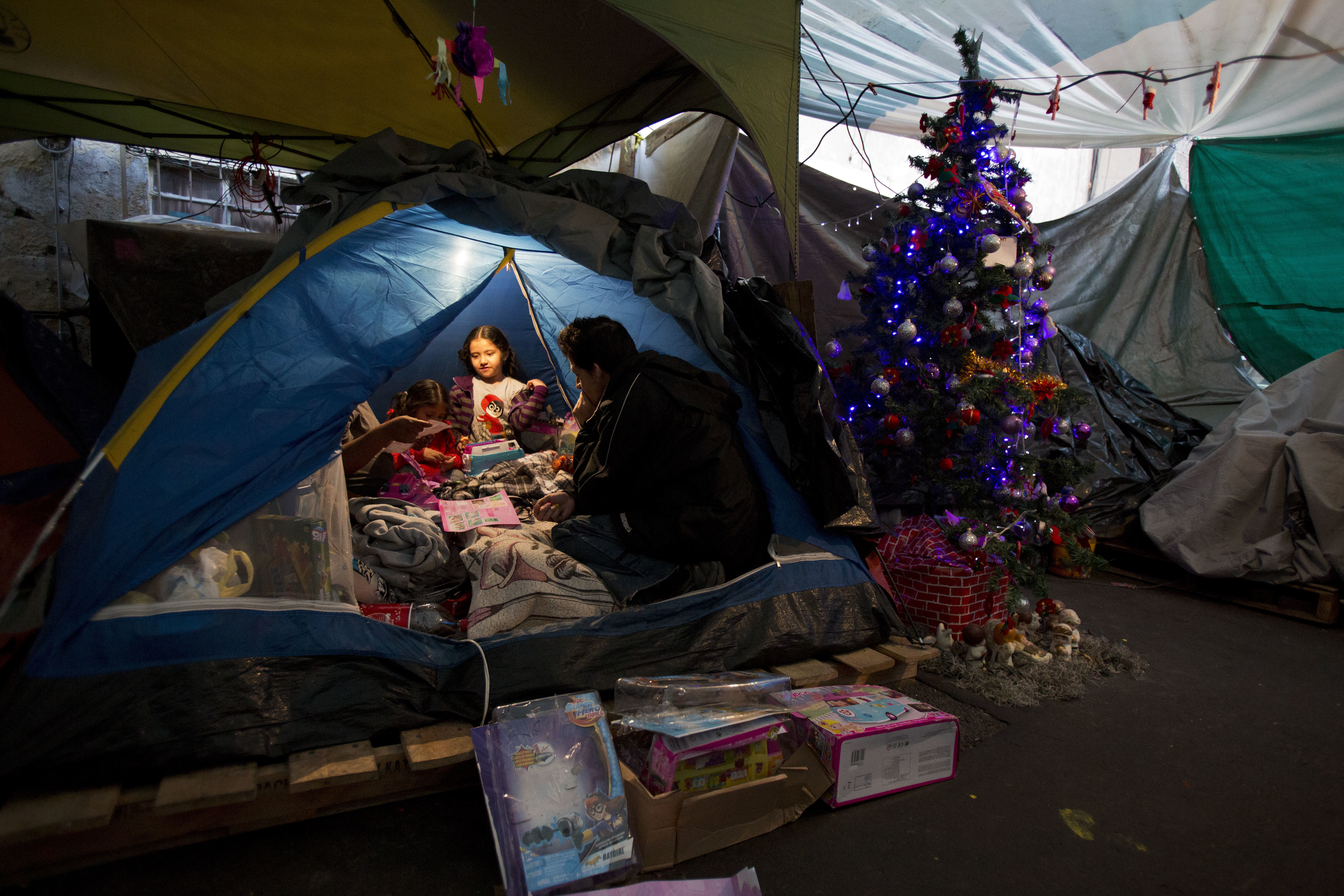 Julio Dominguez Lozara, 33, looks on from the edge of the tent as his daughter Cynthia, 7, and her two sisters play with Three Kings Day gifts in the tent camp where they are living outside of their apartment that was damaged in the September earthquake in Mexico City, Saturday, Jan. 6, 2018. In Mexico, it is customary for people to give gifts on Three Kings Day every Jan. 6, rather than Christmas day. According to Christian tradition, Jan. 6 marks the arrival of three wise men bearing gifts for the baby Jesus. (AP Photo/Rebecca Blackwell)
