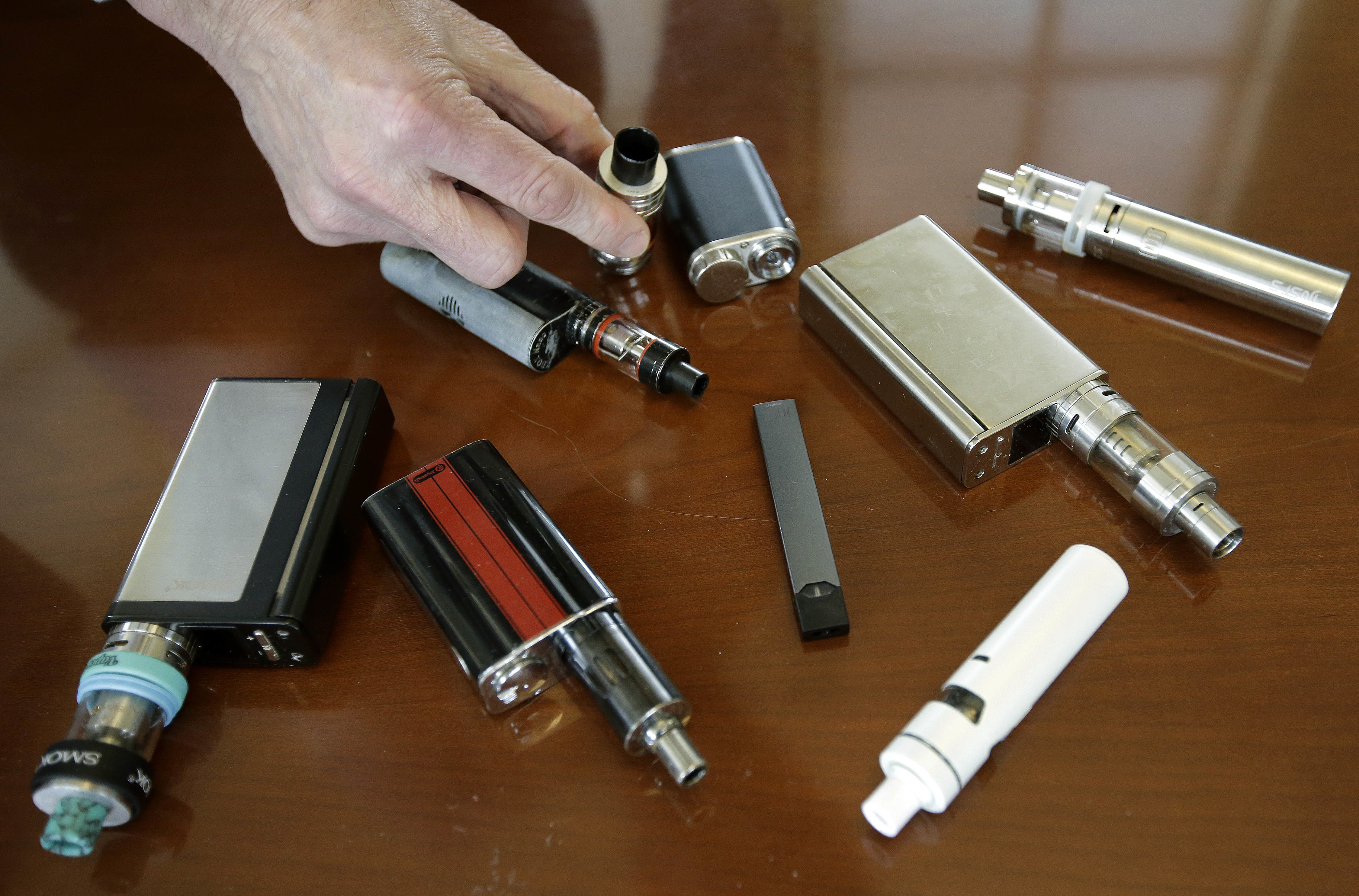 In this Tuesday, April 10, 2018 photo Marshfield High School Principal Robert Keuther displays vaping devices that were confiscated from students in such places as restrooms or hallways at the school in Marshfield, Mass. Health and education officials across the country are raising alarms over wide underage use of e-cigarettes and other vaping products. The devices heat liquid into an inhalable vapor that's sold in sugary flavors like mango and mint, and often with the addictive drug nicotine. (AP Photo/Steven Senne)