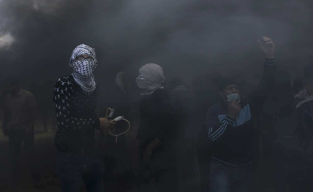 Palestinian protesters hurl stones at Israeli troops while engulfed in smoke from burning tires near the Gaza Strip's border with Israel, east of Khan Younis, in the Gaza Strip, Monday, May 14, 2018. Israeli fire has killed dozens of Palestinians during mass protests along the Gaza border, marking the deadliest day of violence since a devastating 2014 cross-border war and casting a pall over Israel's festive inauguration of the new U.S. Embassy in contested Jerusalem. (Adel Hana, AP Photo)