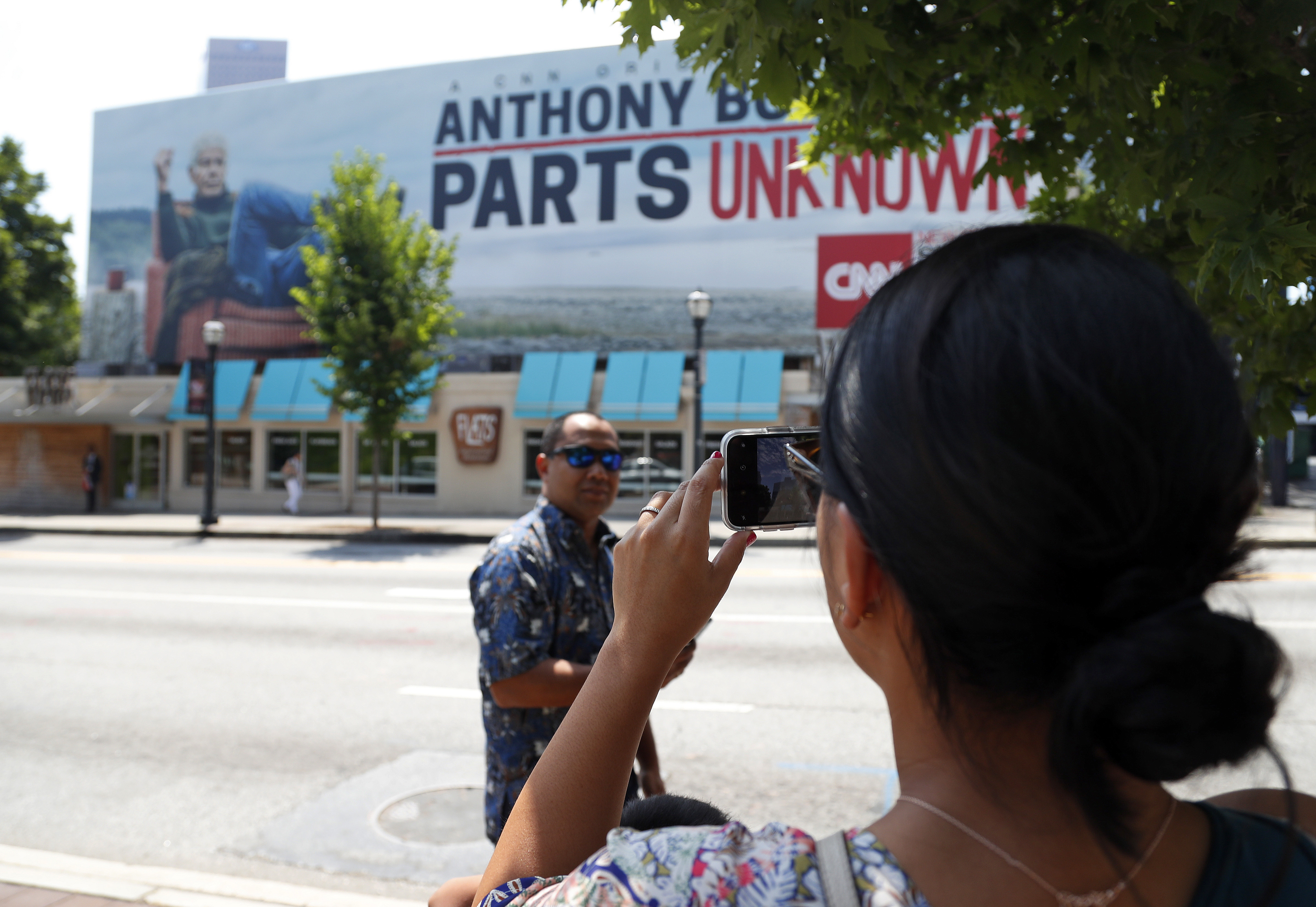 A woman takes a photograph of a billboard for the CNN television show "Parts Unknown" with American celebrity chef Anthony Bourdain, Friday, June 8, 2018 in Atlanta. Bourdain, 61, was found dead in his hotel room in France on Friday, while working on the series which features culinary traditions around the world. (AP Photo/John Bazemore)
