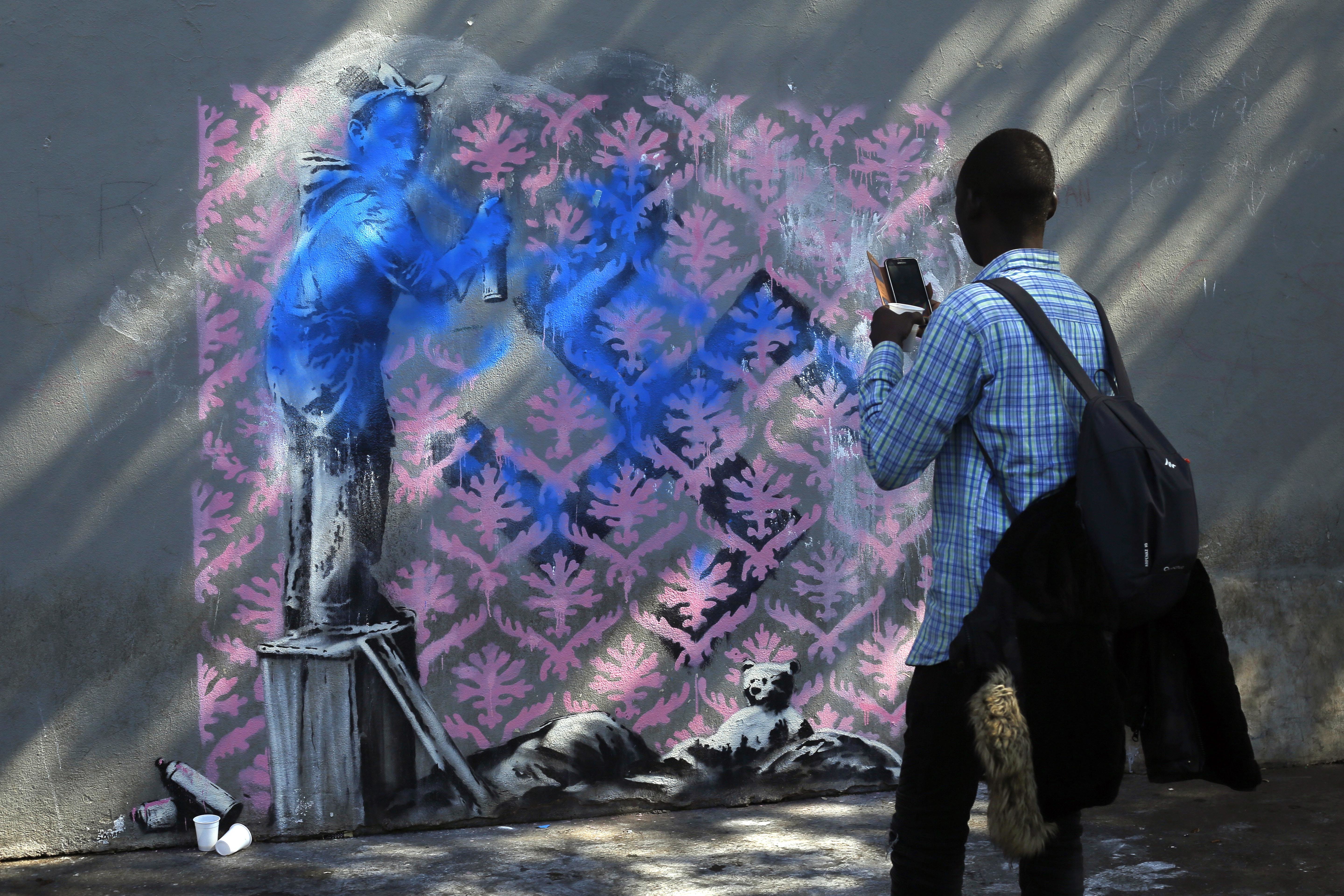 A migrant takes a picture of a graffiti believed to be attributed to street artist Banksy, in Paris, Monday, June 25, 2018. Photo: Thibault Camus, AP Photo