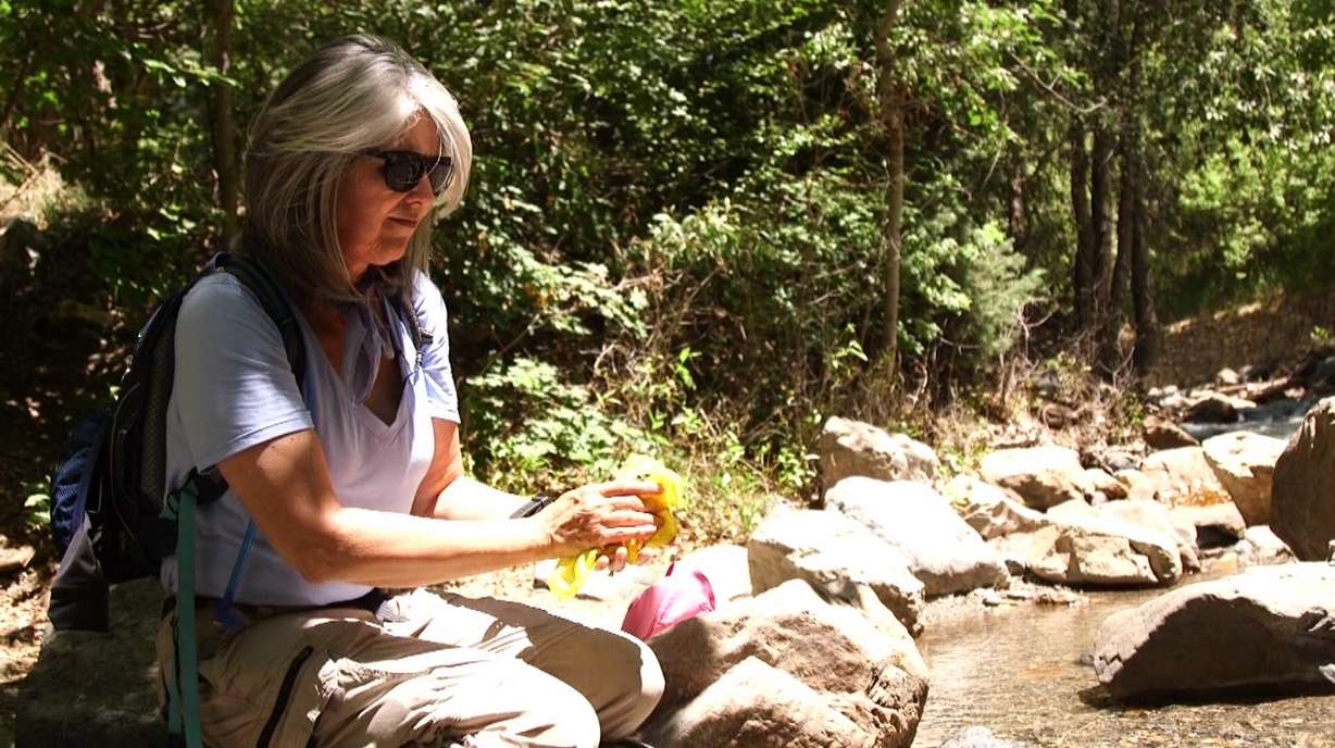 Sue Leininger sits neat a stream and dips an extra bandanna in the water to wipe her arms and face down when she gets too hot. (Photo: KSL TV)