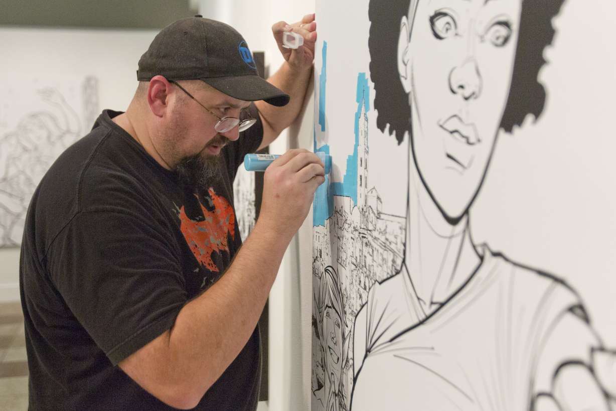 Chad Hardin tests out a paint marker on one of the canvas images at the Woodbury Art Museum at University Place on Friday, July 27, 2018, in Orem, Utah. (Evan Cobb, The Daily Herald via AP)