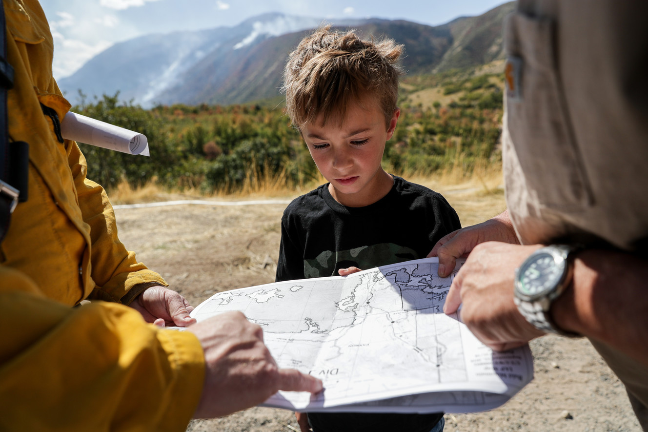 Dennis Jacobson, right, and his grandson, Tripp Peacock, 8, look at a map of fire lines with Lone Peak Fire Chief Reed Thompson, left, after Jacobson was able to return to his home in Elk Ridge after evacuations were lifted on Saturday, Sept. 22, 2018. (Photo: Spenser Heaps, KSL)