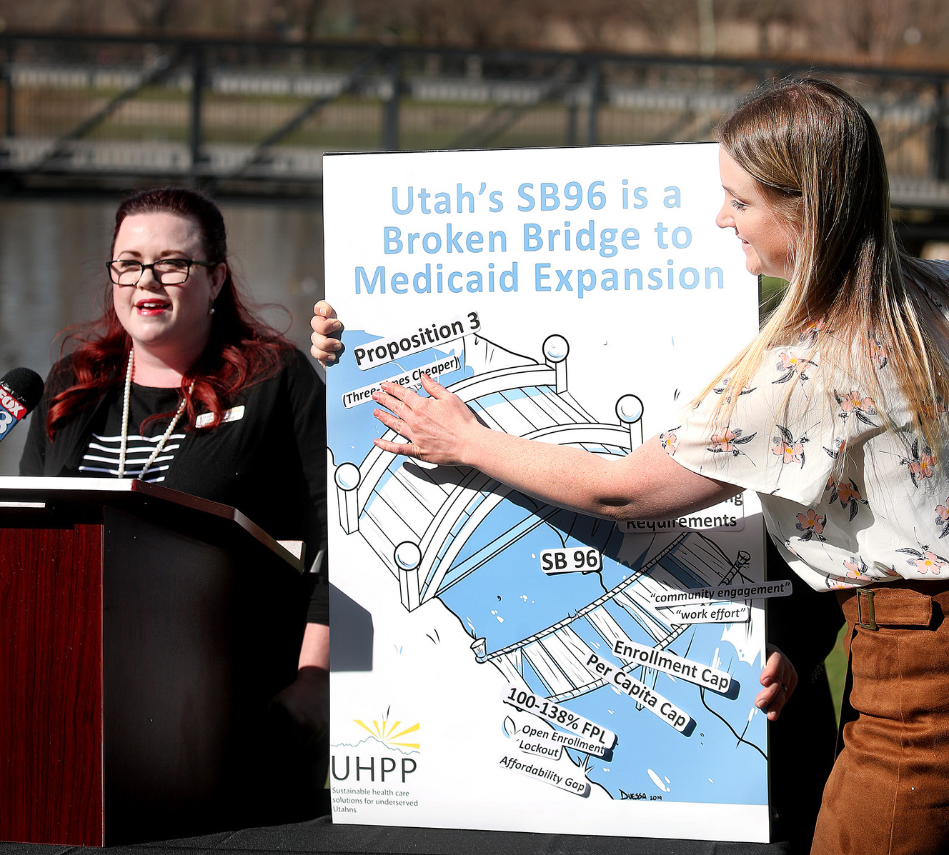 Stacy Stanford, of the Utah Health Policy Project, speaks during a press conference at Liberty Park in Salt Lake City on Monday, April 1, 2019, as Courtney Bullard places tags on a board highlighting areas where Utahns will be left behind through the state's partial Medicaid expansion plan. (Photo: Scott G Winterton, KSL)