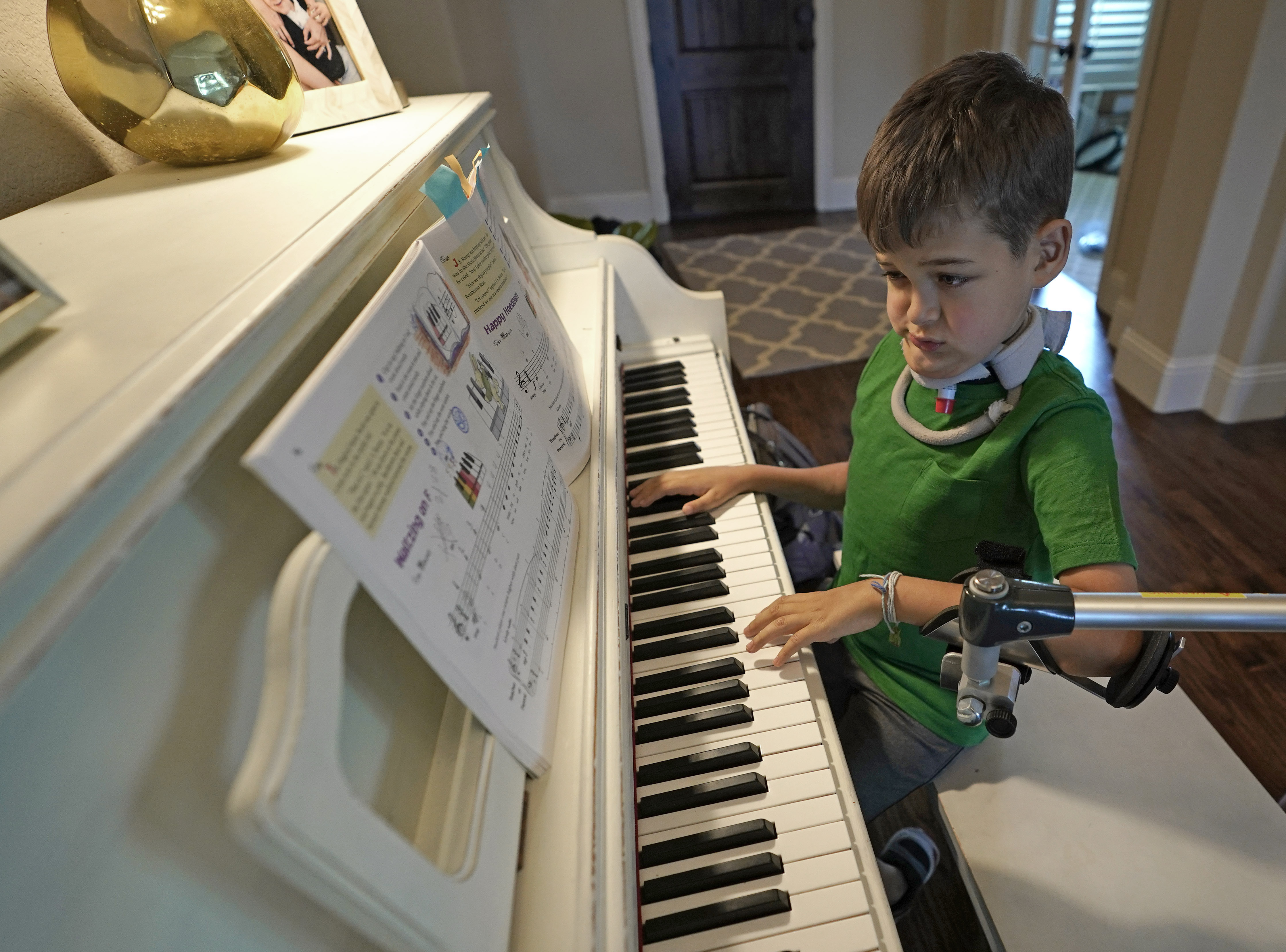 Braden Scott uses a device to support his left arm as he practices on the piano in Tomball, Texas on Friday, March 29, 2019. Photo: David J. Phillip, AP Photo
