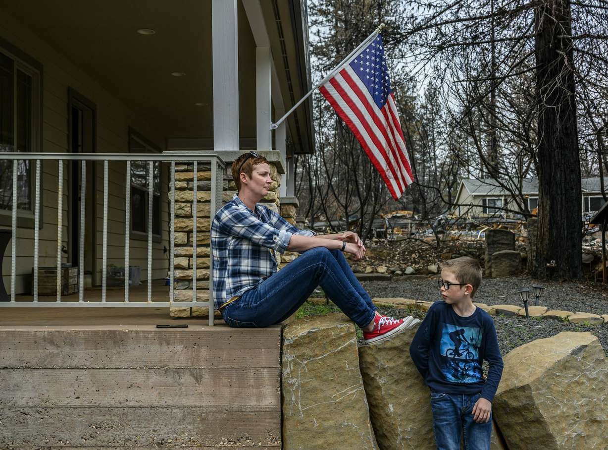 In this photo taken March 19, 2019, Dawn Herr and her son Liam, 8, visit their home in Paradise, Calif., that survived the Camp Fire. The Herrs' home, built in 2010, was scorched and had smoke damage inside so the family is living temporarily in nearby Chico. The Herrs credit the home’s survival to strict building codes and to gravel that encircled the building and kept the flames back. (Hector Amezcua/The Sacramento Bee via AP)