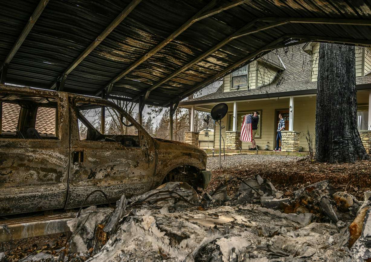 In this March 19, 2019, Sean and Dawn Herr collect an American flag that survived the Camp Fire along with their Paradise, Calif., home. The Herrs' home, built in 2010, was scorched and had smoke damage inside so the family is living indefinitely in nearby Chico. The Herrs credit the home’s survival to strict building codes and to gravel that encircled the building and kept the flames back. (Hector Amezcua/The Sacramento Bee via AP)